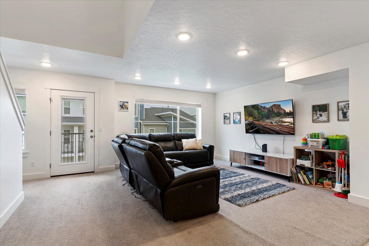 Spacious living area featuring neutral carpeting, recessed ceiling lighting, a large window, a glass-paneled exterior door, and a built-in media console