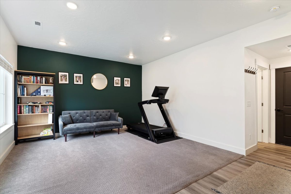 Spacious room featuring a dark accent wall, recessed lighting, neutral carpeting, and wood-finish flooring at the entry