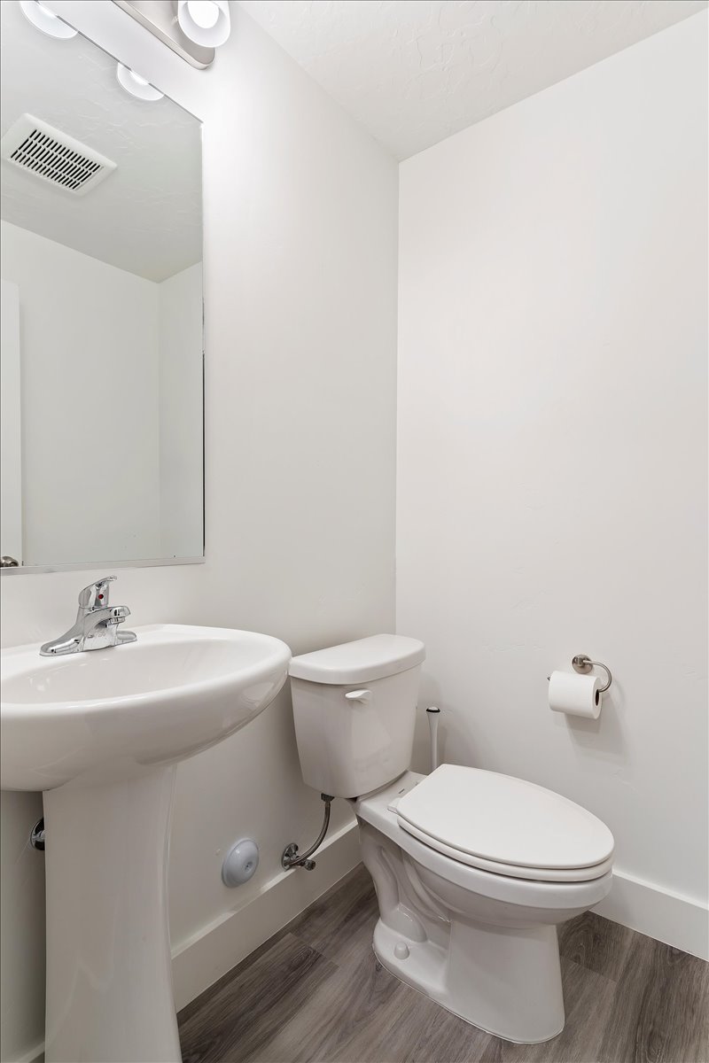 Powder room featuring a pedestal sink with chrome faucet, a white toilet, and wood-finish flooring