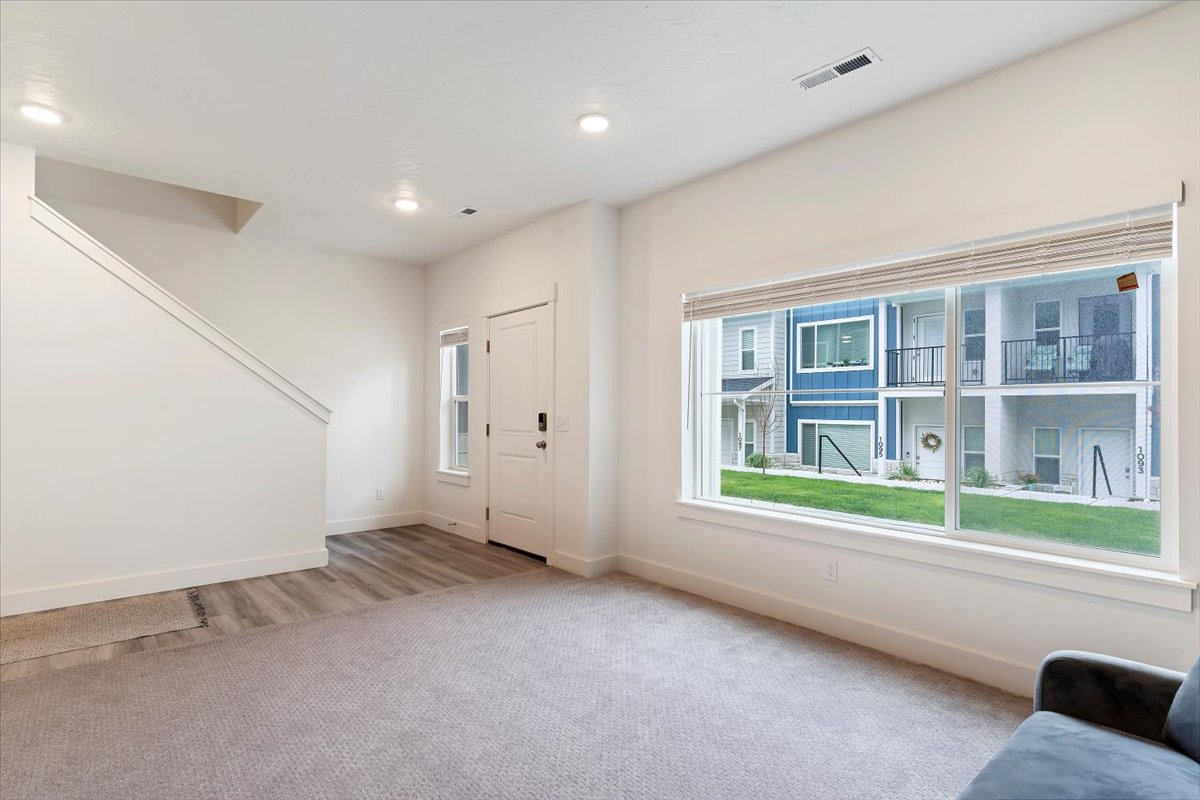 Open-concept room featuring a large picture window, recessed lighting, neutral carpet, wood-finish flooring, and a white entry door