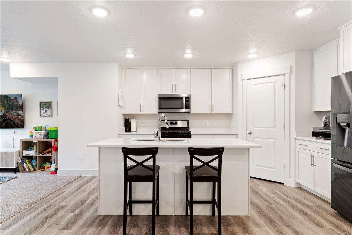 Modern kitchen featuring white cabinetry, a central island with countertop seating, stainless steel appliances, recessed lighting, and wood-finish flooring