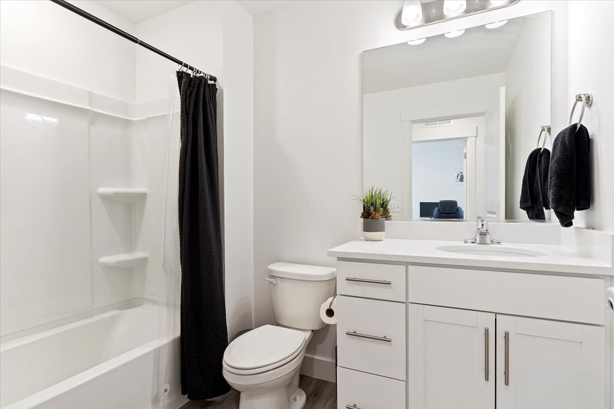 Bathroom featuring a white vanity with brushed nickel hardware, a white countertop, a rectangular mirror, and a full-size bathtub with a shower