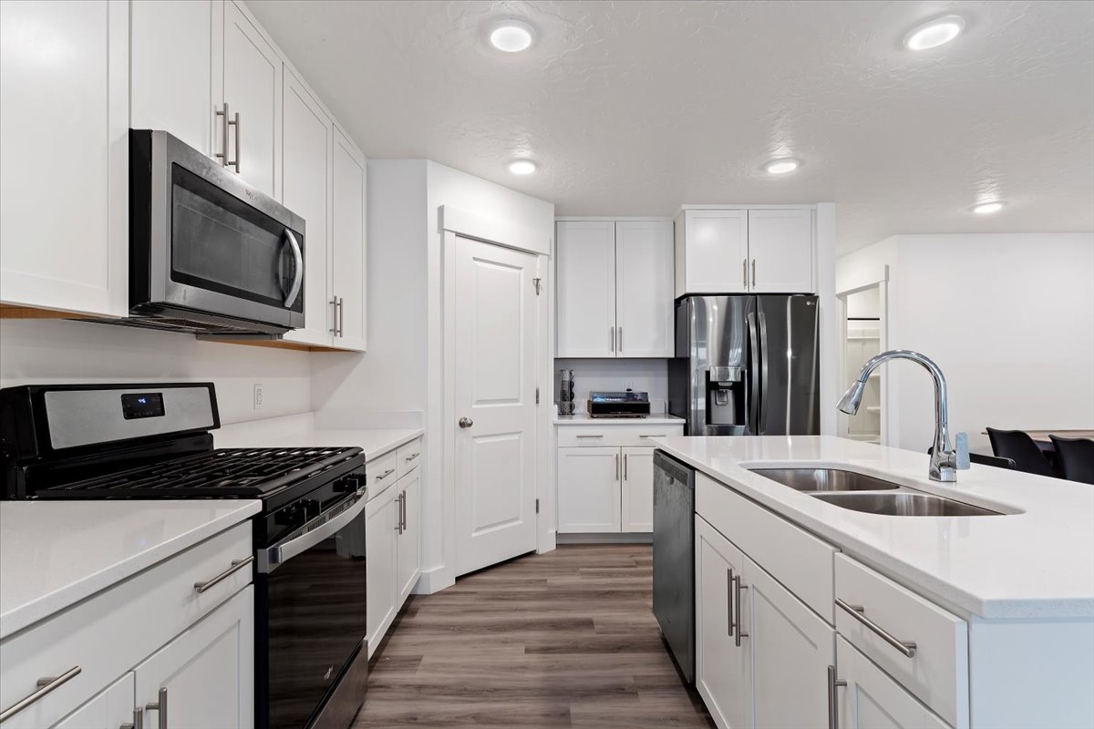 Modern kitchen featuring white shaker cabinetry, stainless steel appliances, a center island with a double sink, and wood-finish flooring