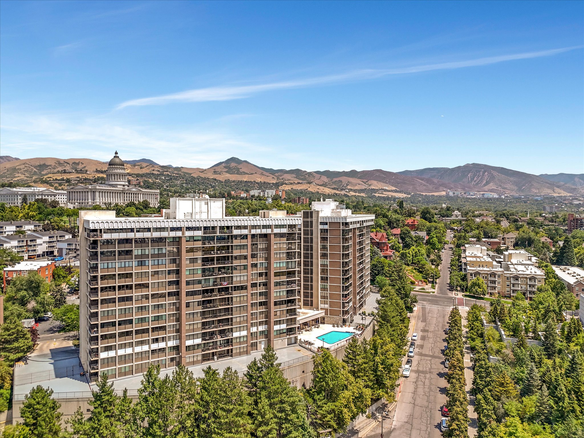 High-rise residential complex featuring a multi-story facade with balconies, an outdoor swimming pool, and mature tree-lined streets