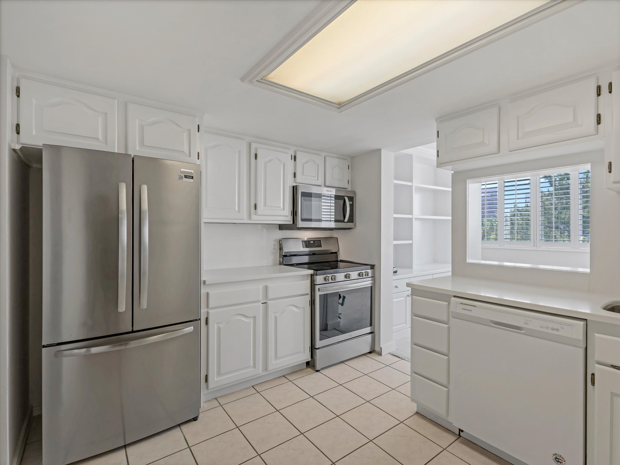 Kitchen featuring white cabinetry, quartz countertops, stainless steel appliances, tile flooring, and a pass-through window