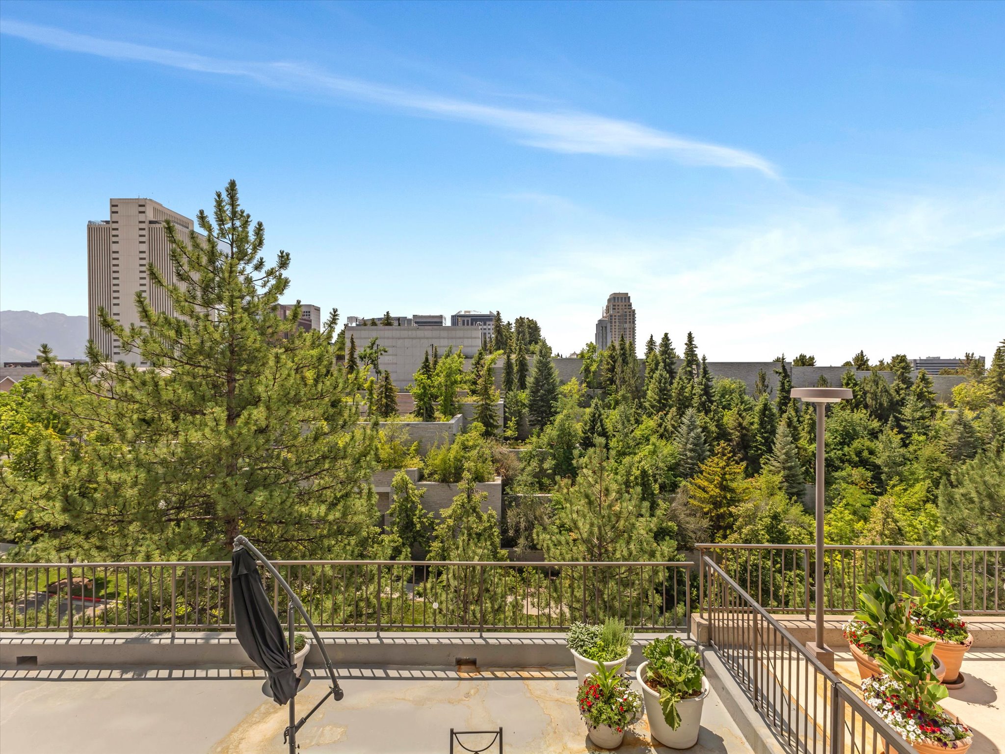 Spacious outdoor terrace with a metal railing system, concrete flooring, and surrounded by an alpine granite scape and theSLC Downtown skyline