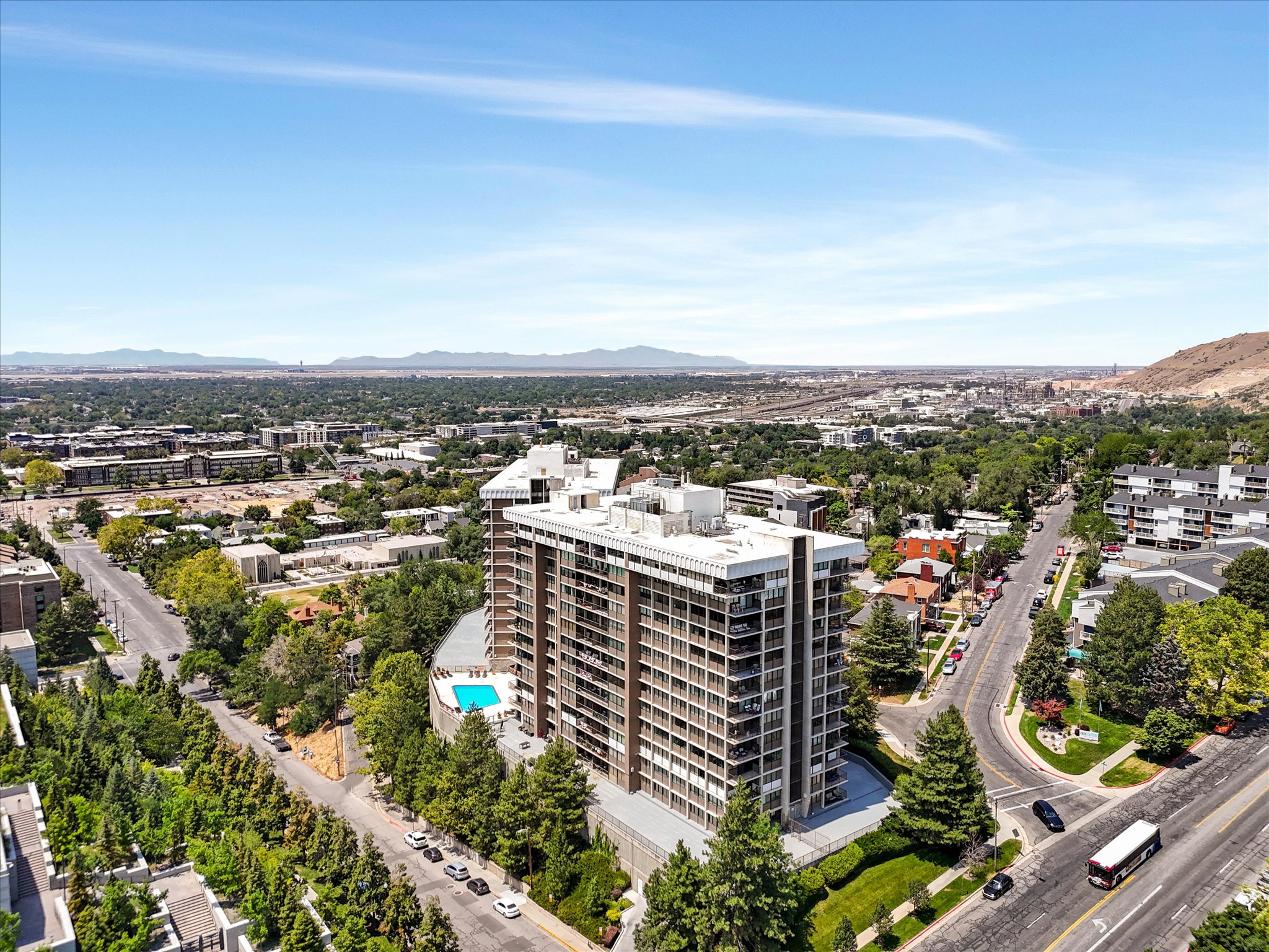High-rise building featuring multiple levels of balconies, an outdoor swimming pool, and surrounding mature landscaping