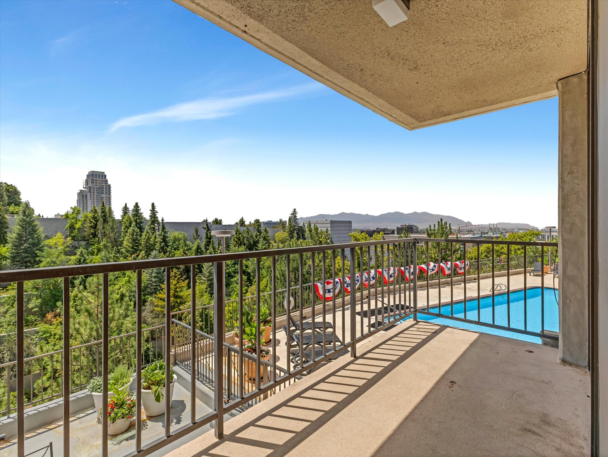 Expansive balcony with concrete flooring and a dark metal railing, overlooking a sparkling salt water swimming pool and sweeping valley and Oquirhh Mountain views