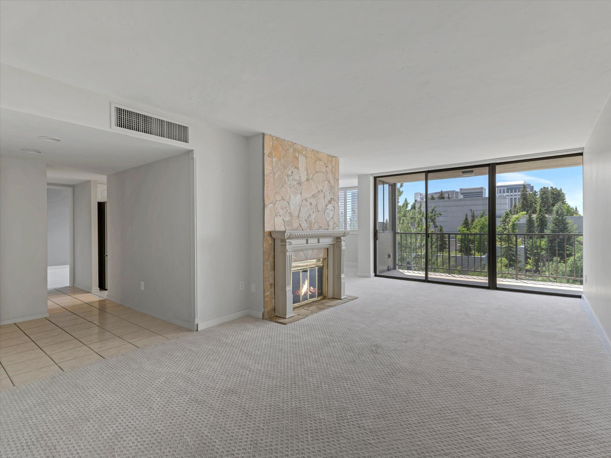 Living area featuring a stone-clad fireplace with a decorative mantel, light-toned carpet flooring, and a sliding glass door opening to a private balcony