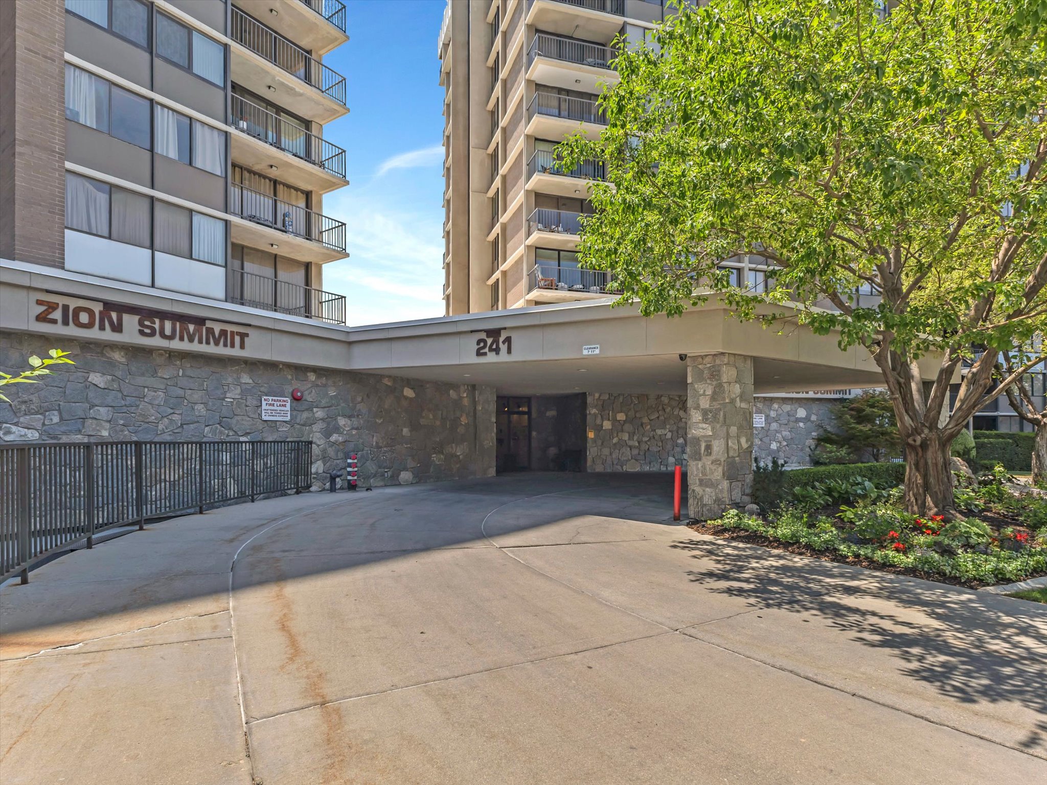 Covered entry drive featuring stone accents and mature landscaping