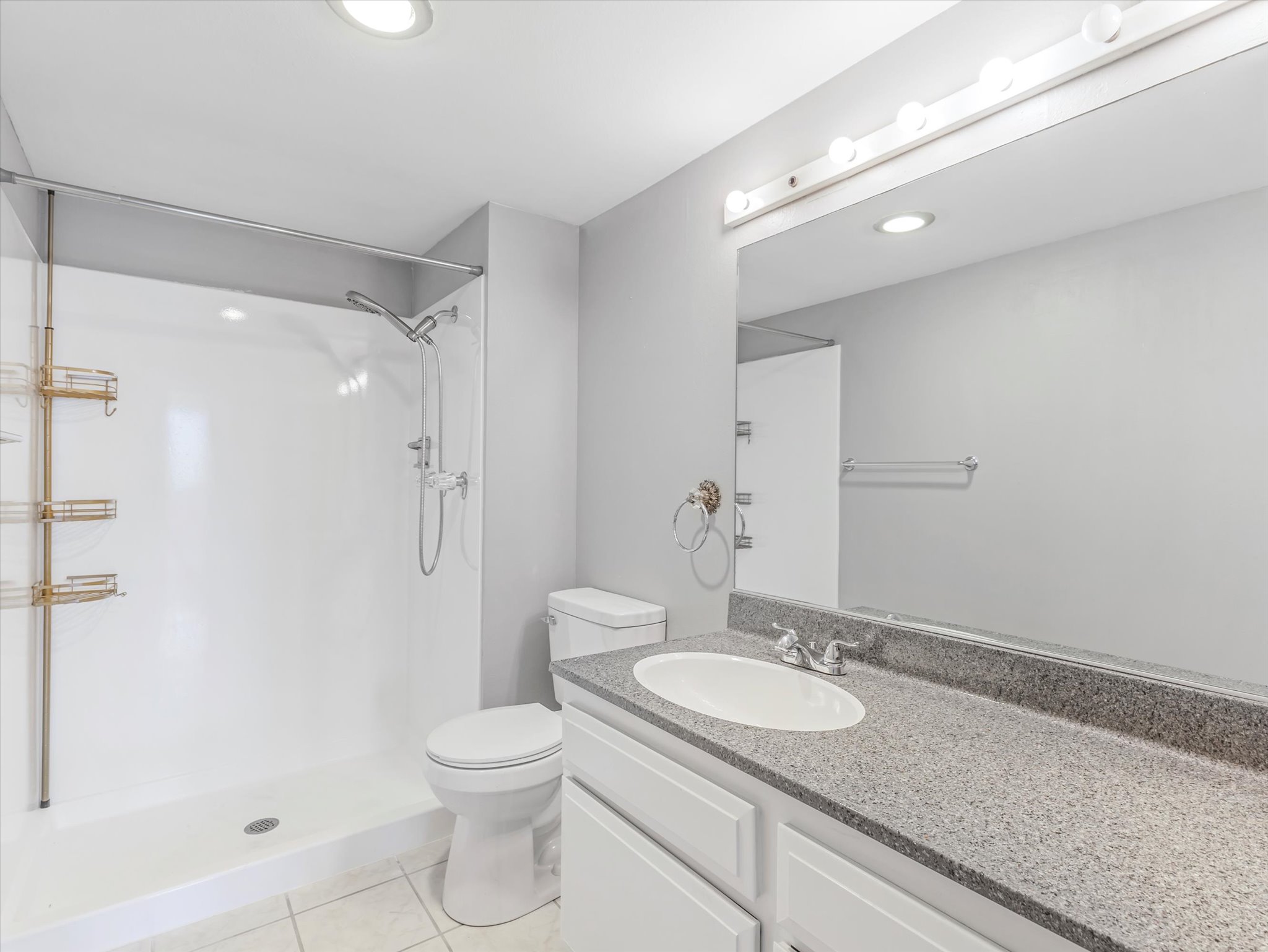Bathroom featuring a white shower with an adjustable showerhead, a toilet, and a vanity with an integrated sink