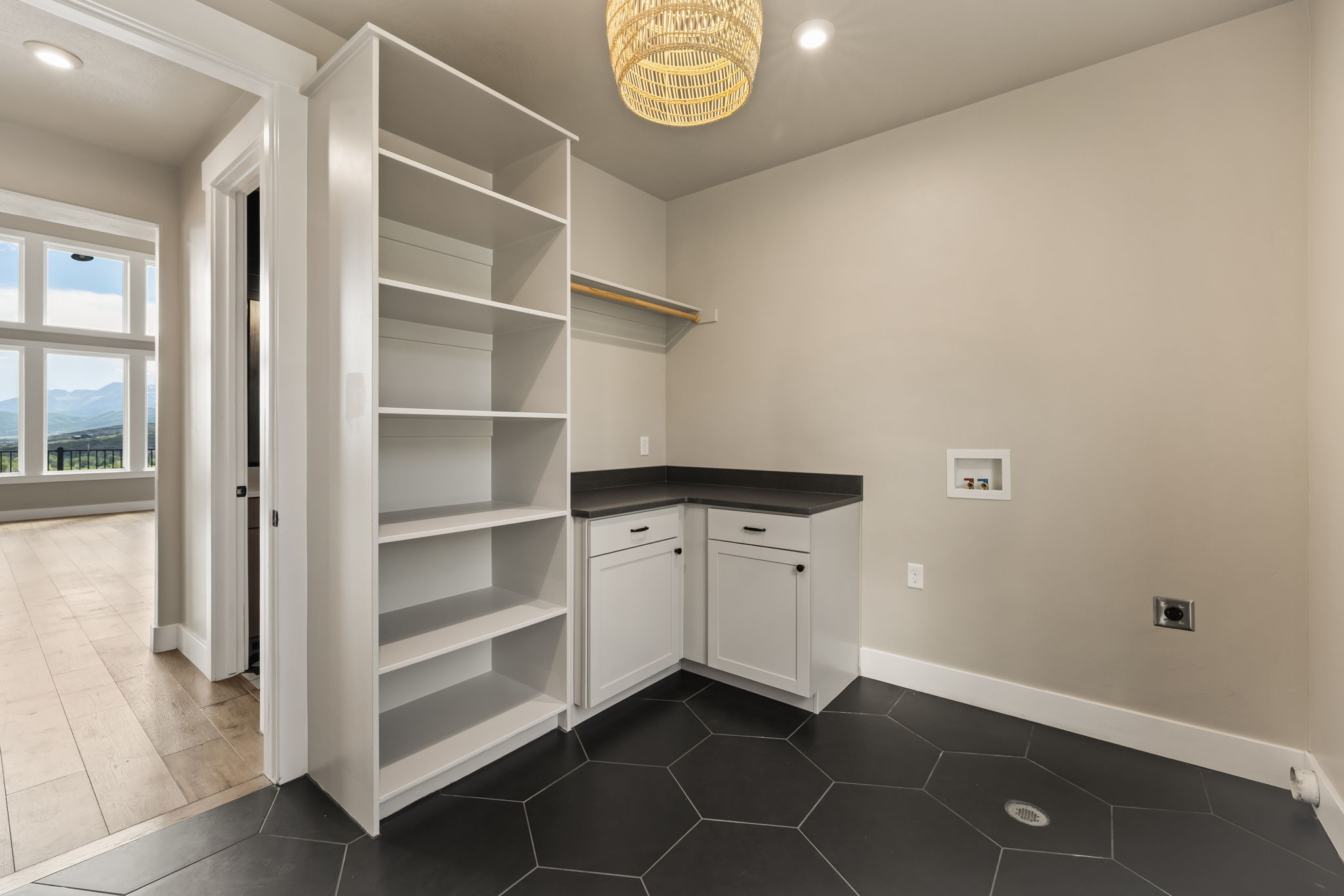 Utility room featuring hexagonal dark tile flooring, built-in open shelving, white cabinetry, dark countertops, and a clothing rod