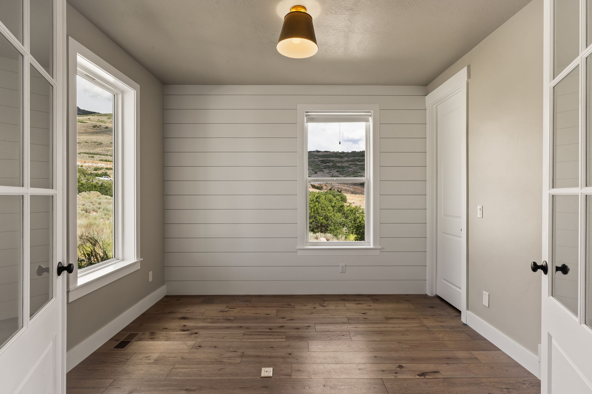 Interior space featuring wood-finish flooring, shiplap accent wall, white trim, and a contemporary ceiling light fixture