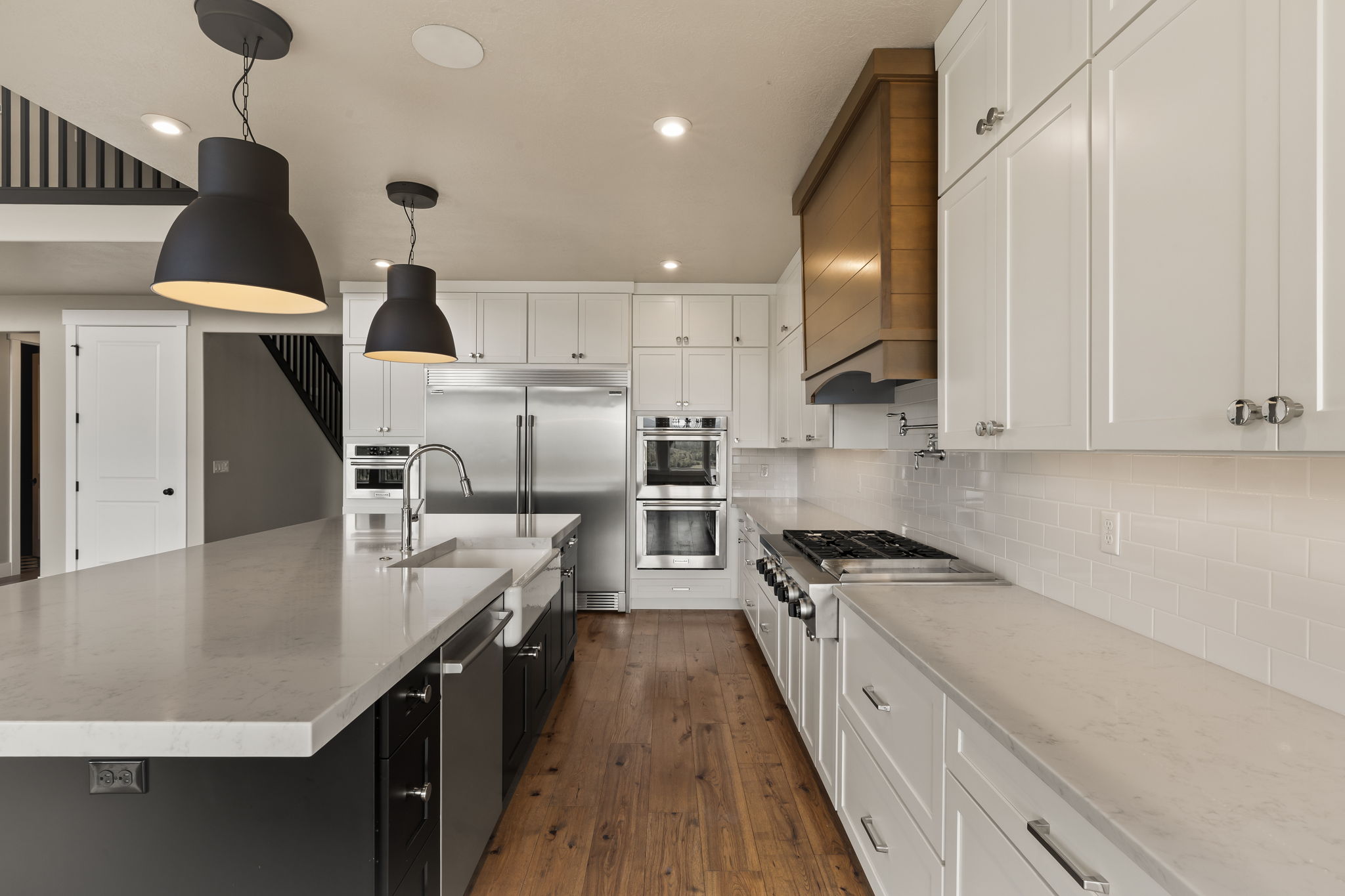 Gourmet kitchen featuring a large central island, light-toned countertops, white shaker cabinetry, stainless steel appliances, and wood-finish flooring