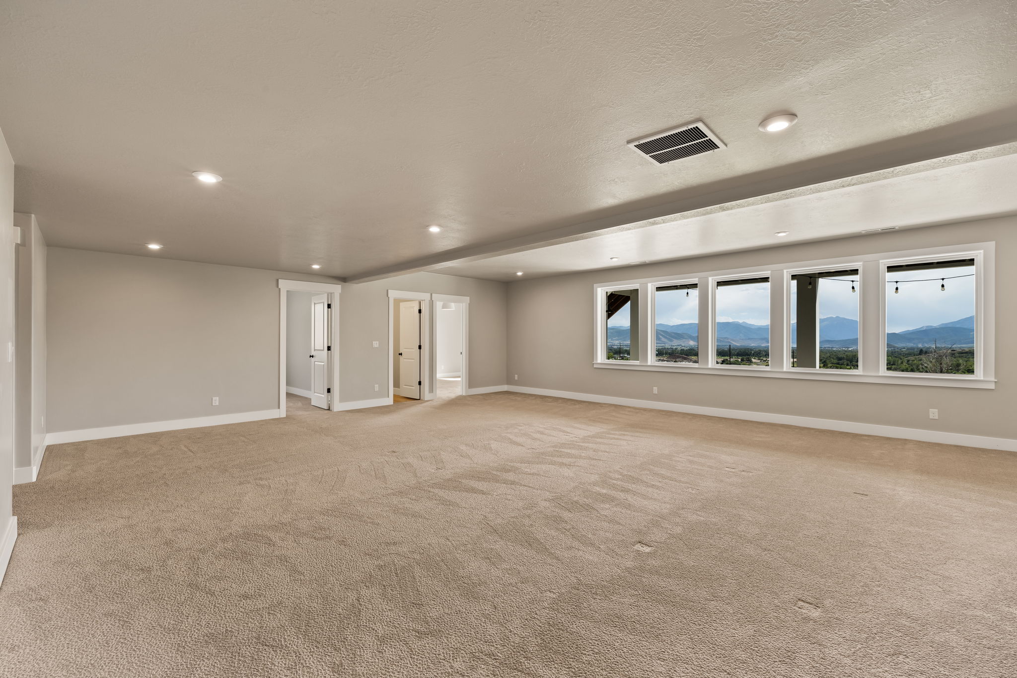 Expansive room featuring a wall of multiple windows showcasing distant mountains and a large, neutral-toned carpeted floor