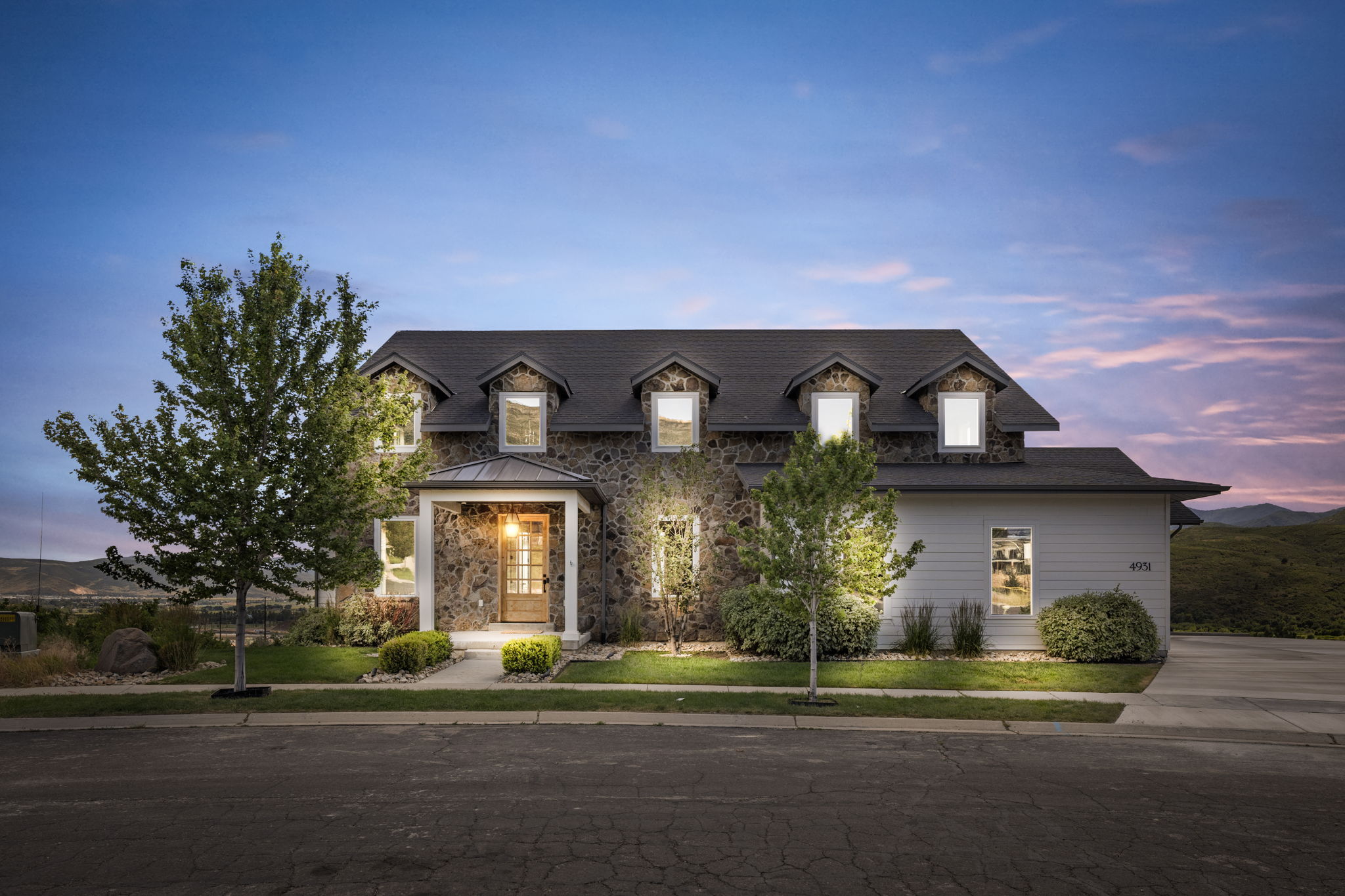Stone and siding exterior with a covered entry, dormer windows, and a black shingle roof