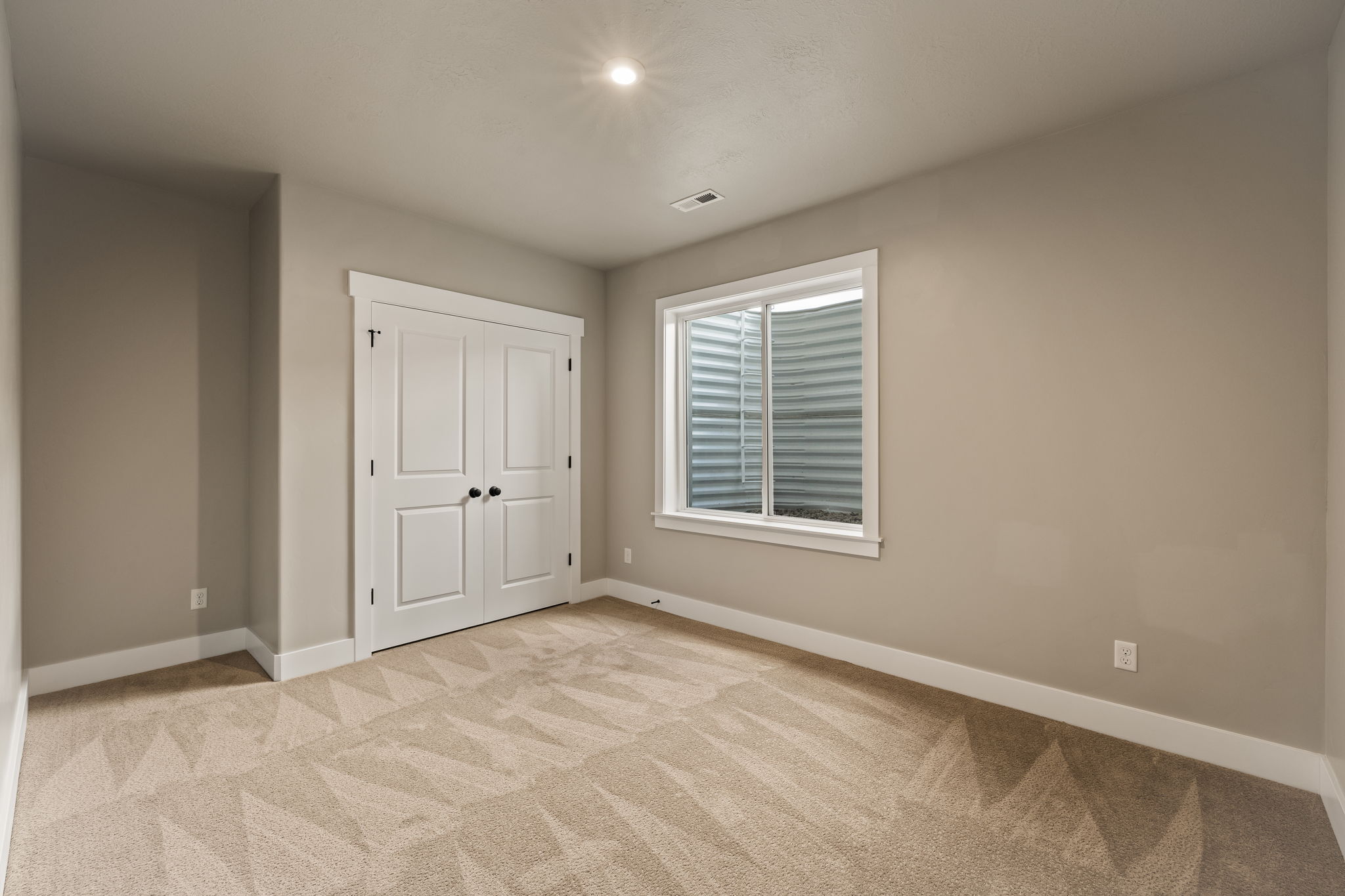 Neutral-toned room featuring a patterned carpet, white trim, and a window with a window well