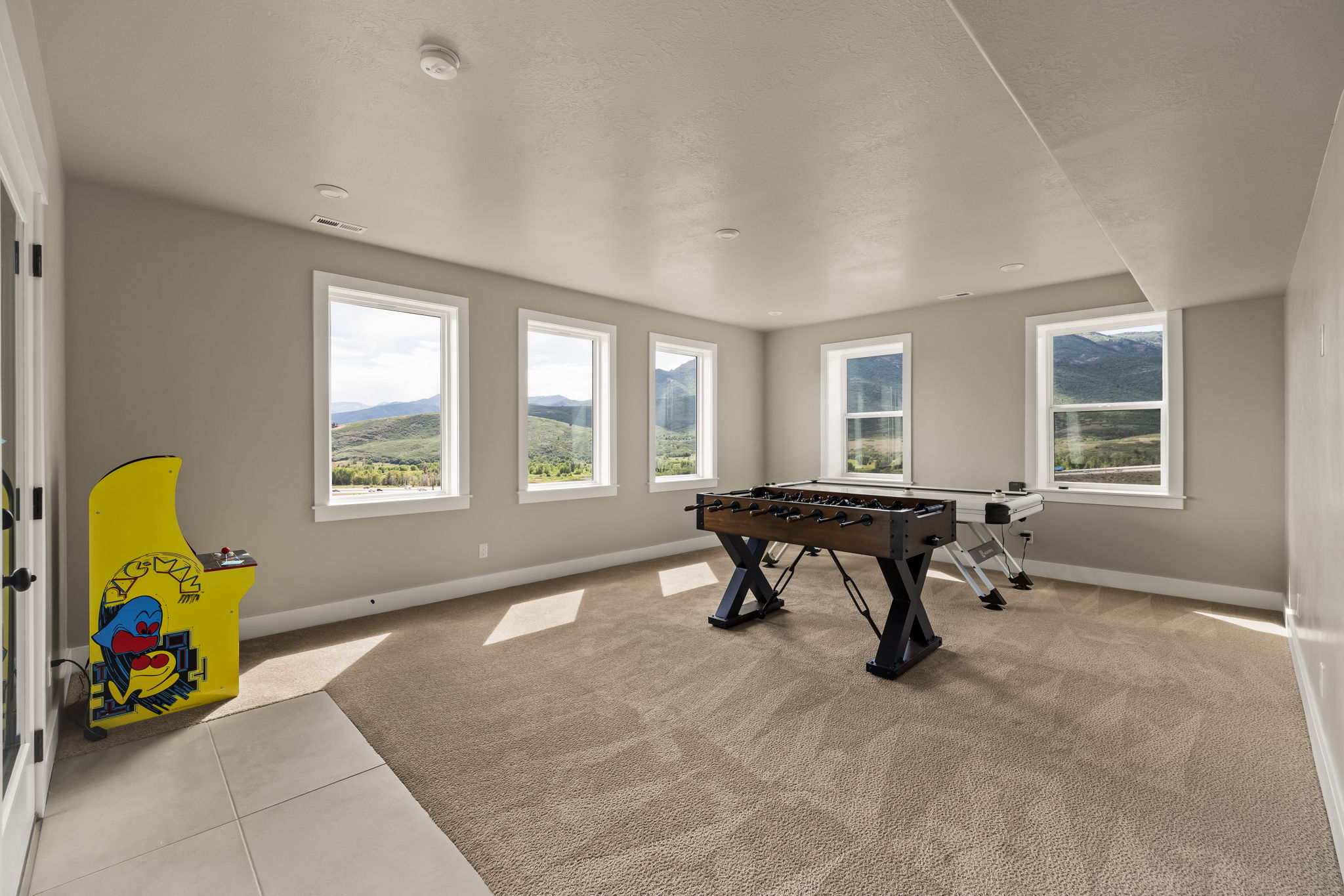 Spacious room with four large windows displaying mountain scenery, light brown carpet, and a section of light-colored tile flooring