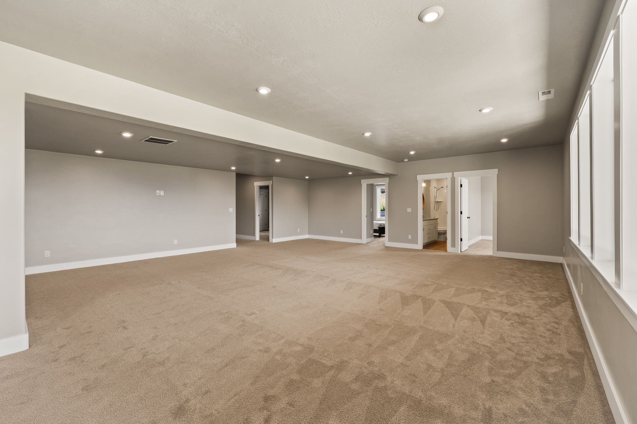 Expansive carpeted room featuring recessed lighting, multiple doorways, and a wall of windows