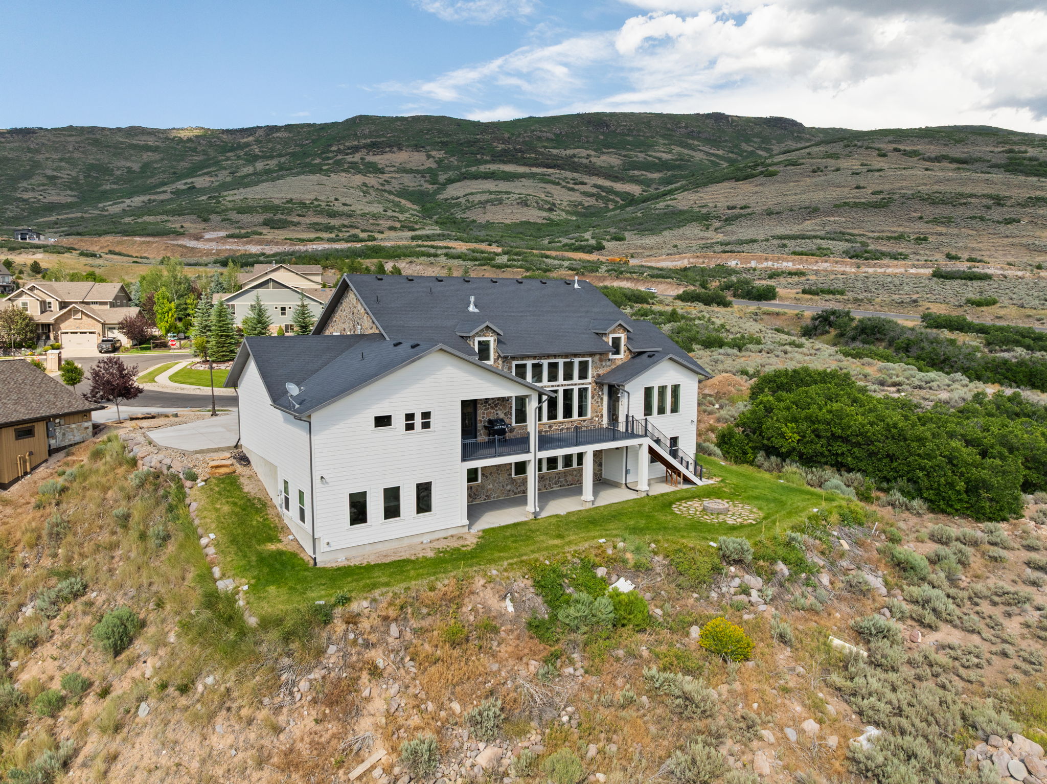 Multi-level residence featuring a dark shingle roof, stone and white siding exterior finishes, and multiple large windows