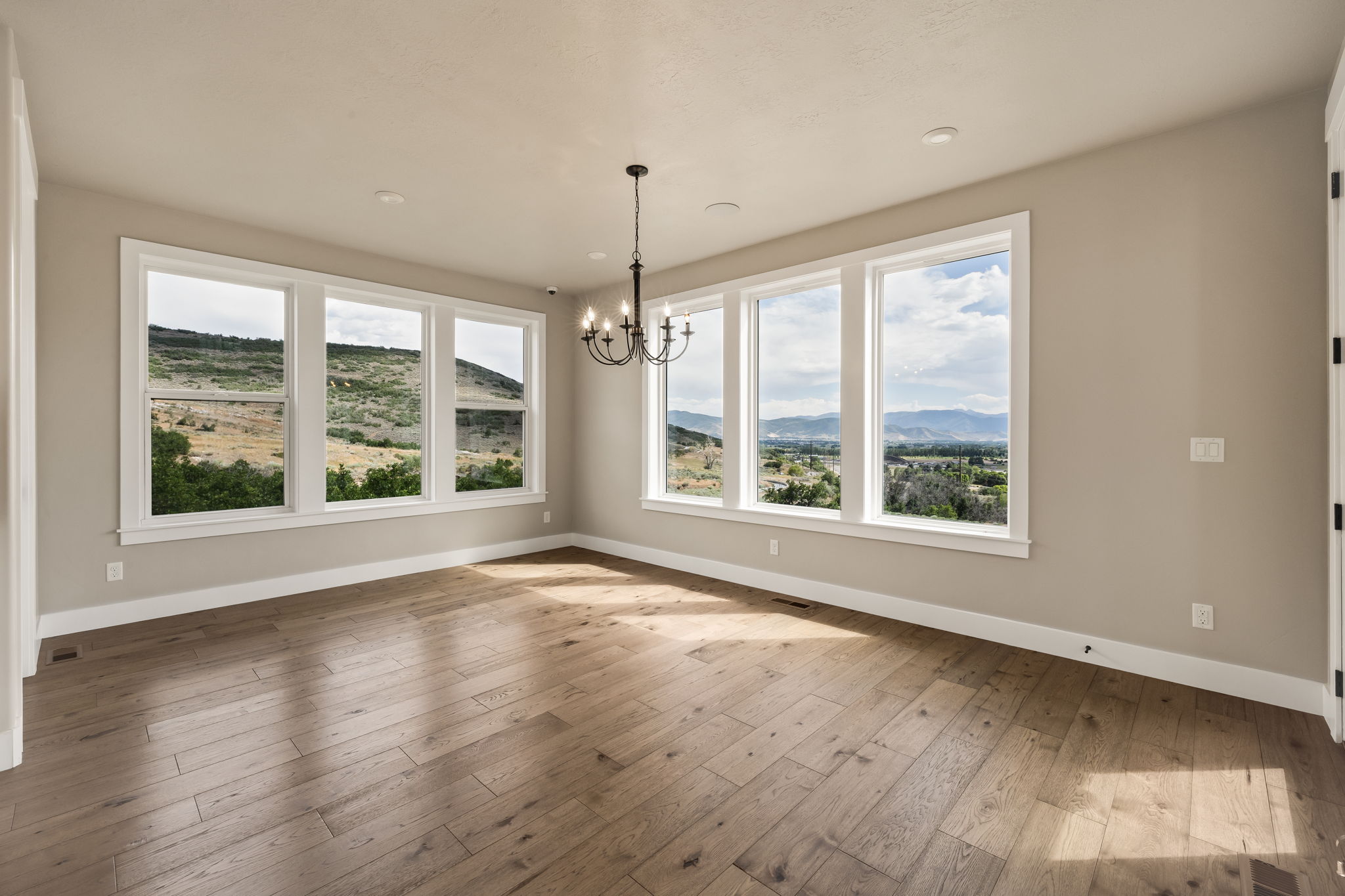 Spacious room featuring multiple large windows, wood-finish flooring, recessed lighting, a chandelier, and neutral wall tones