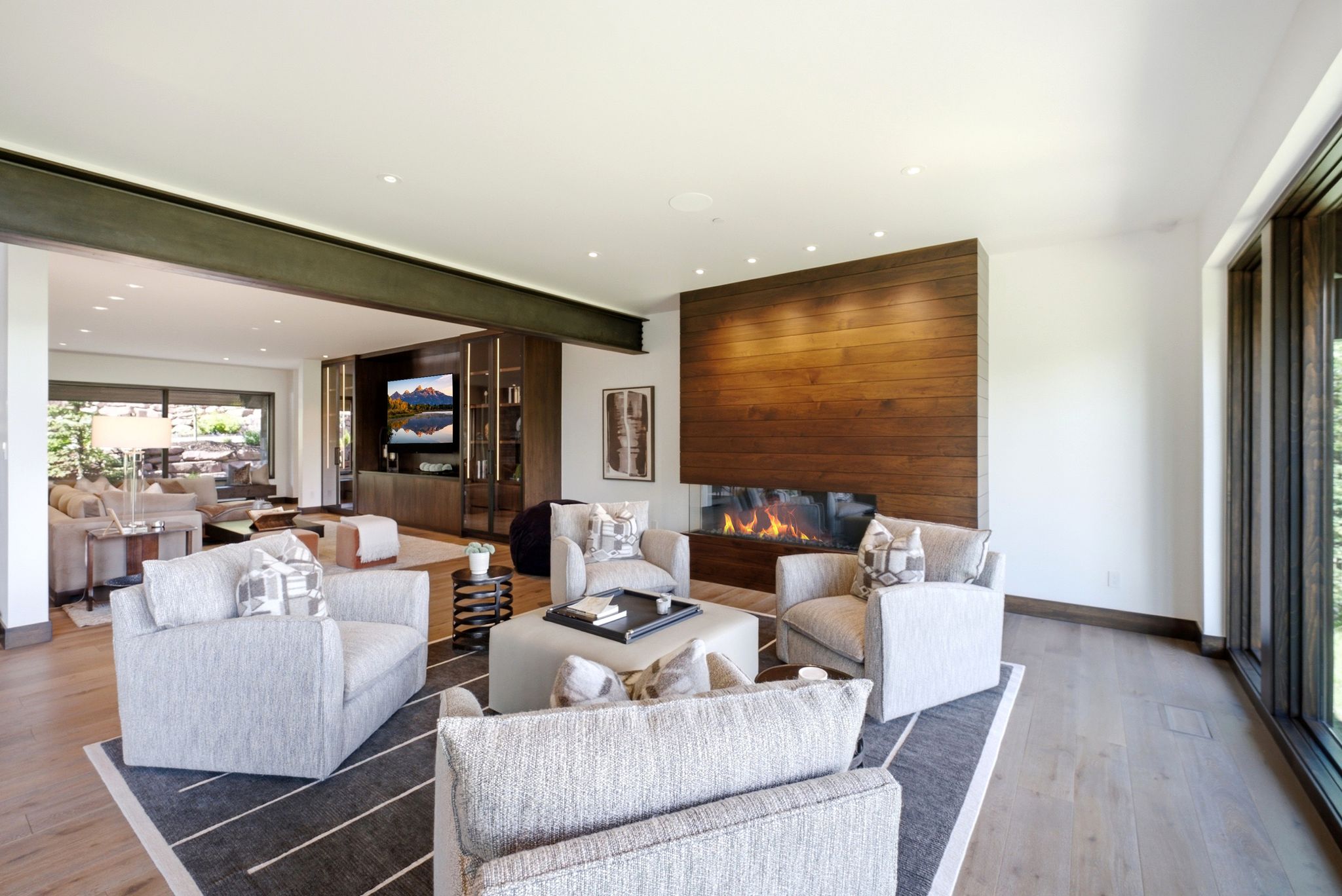 Spacious living area featuring a wood-finish accent wall with a linear fireplace, wood-finish flooring, a full-height window, a recessed lighting scheme, and an exposed structural beam