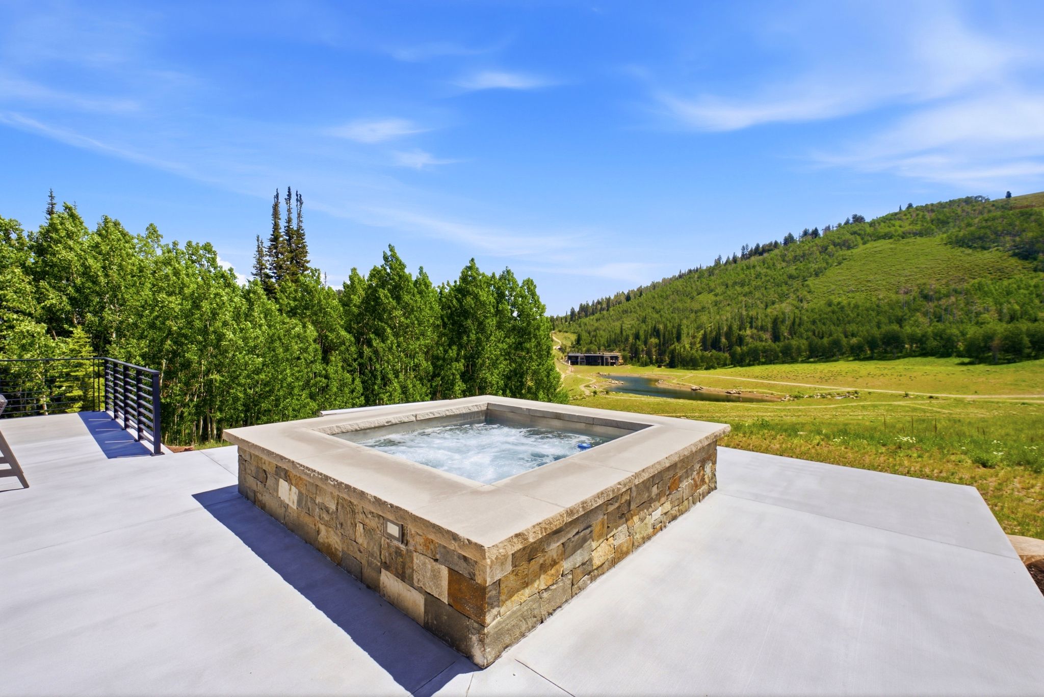 Expansive outdoor patio with a built-in hot tub, natural stone surround, and concrete decking