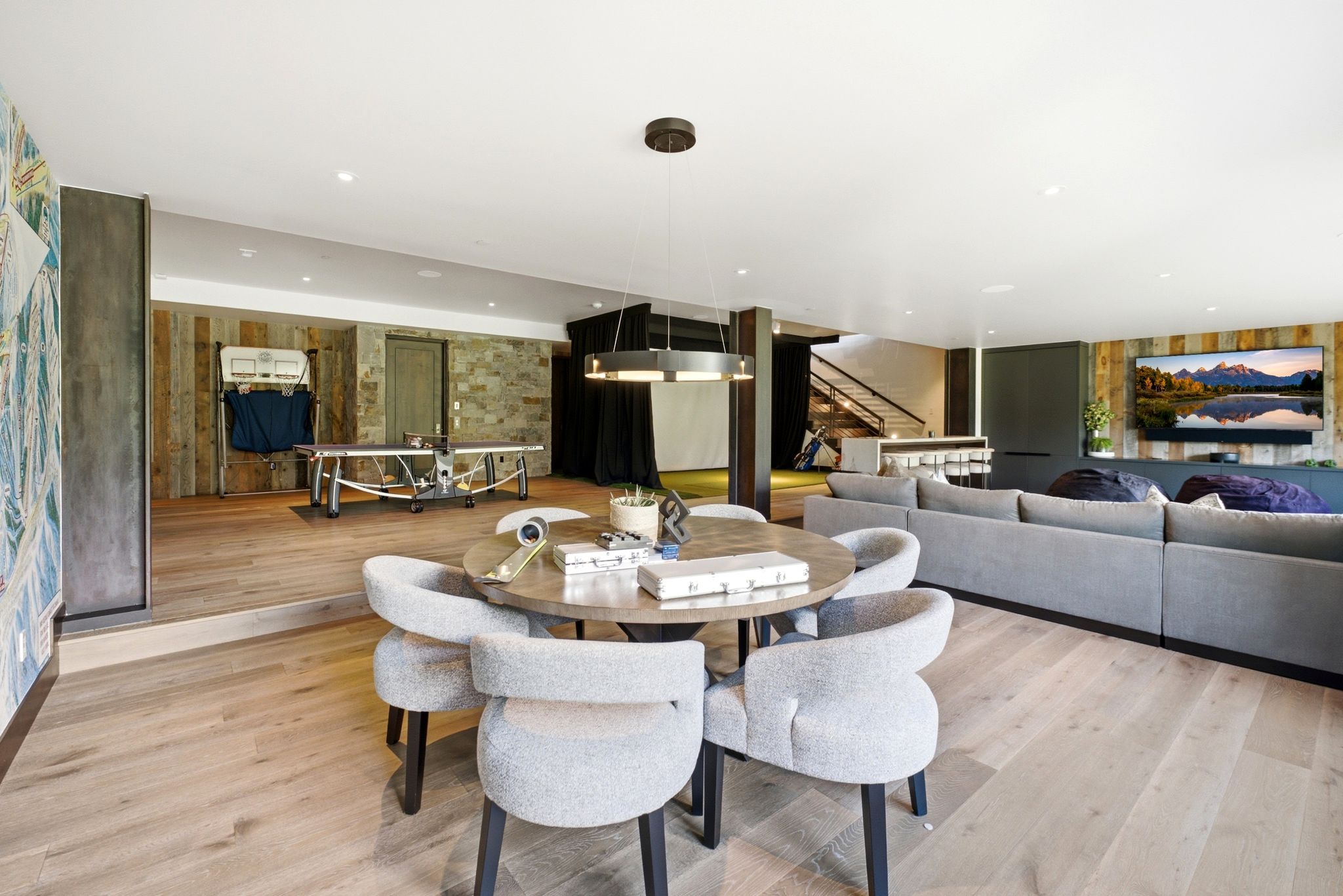 Spacious entertainment area featuring light wood-finish flooring, recessed lighting, and a prominent wood accent wall with a large television