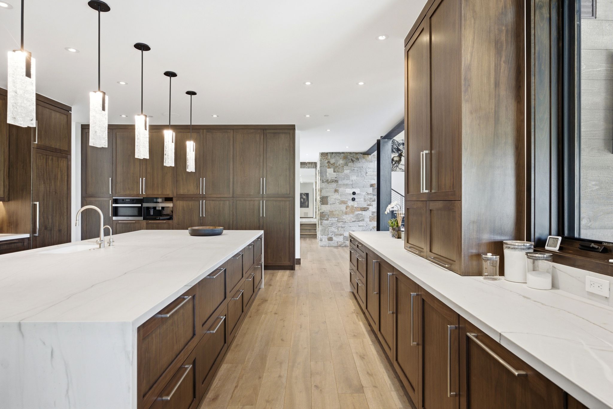 Spacious kitchen with a large central island, extensive dark wood cabinetry, integrated appliances, light wood-finish flooring, and contemporary pendant lighting