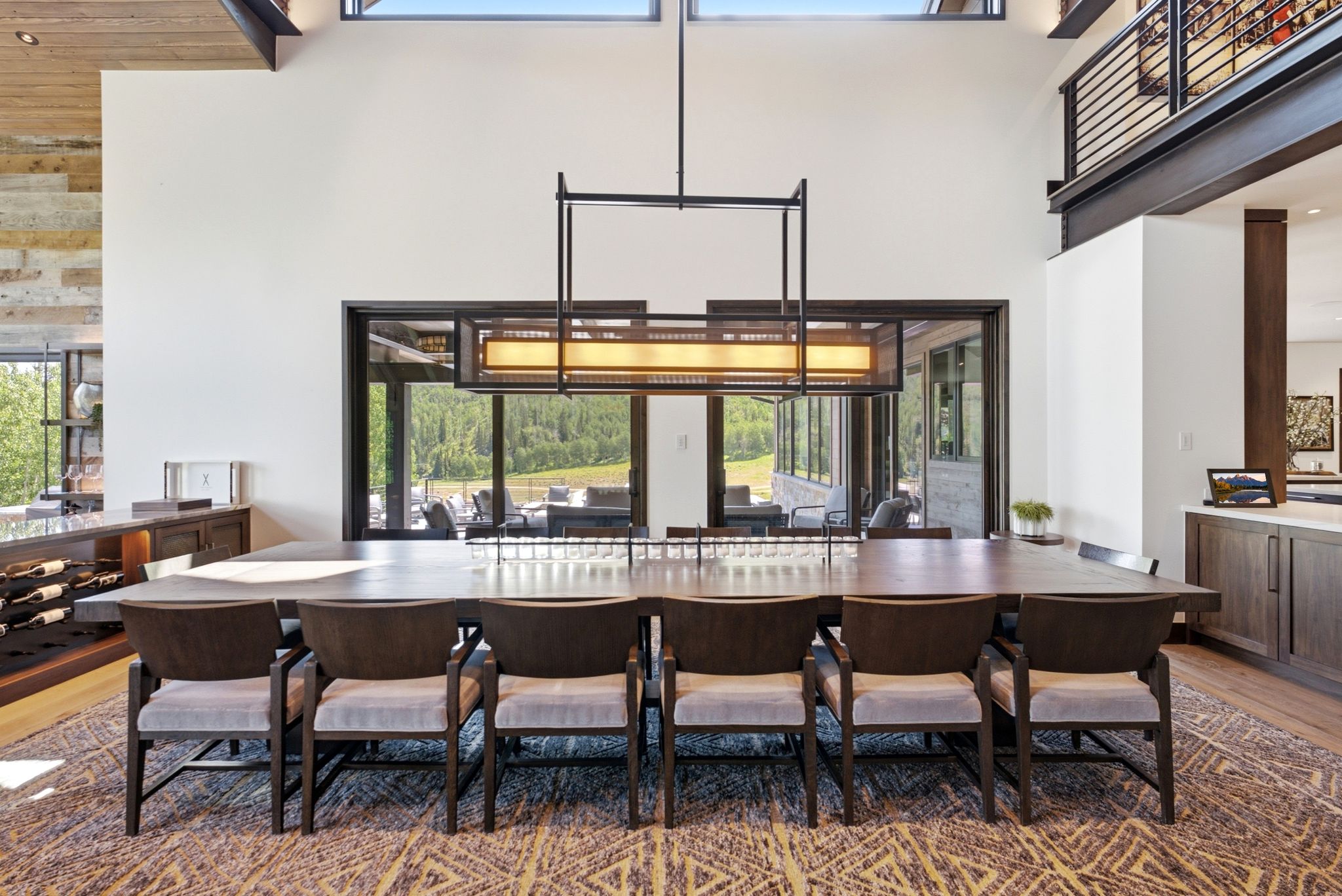 Spacious dining area featuring a vaulted ceiling with exposed beams, an expansive window wall, a linear chandelier, and a built-in wine rack