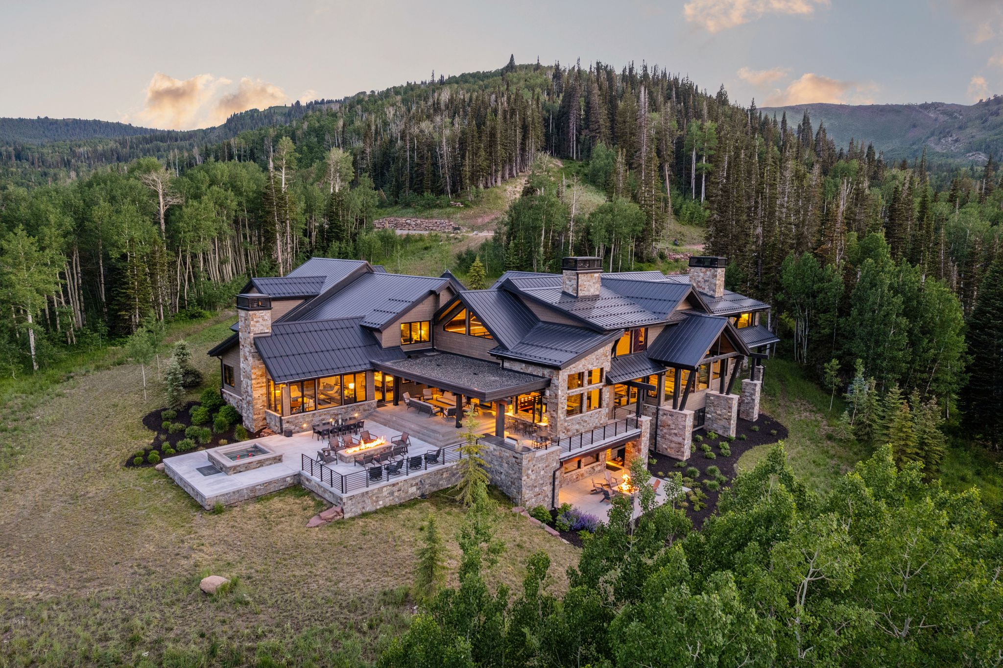 Contemporary mountain-style residence featuring extensive stone veneer, multiple chimneys, and a dark metal roof