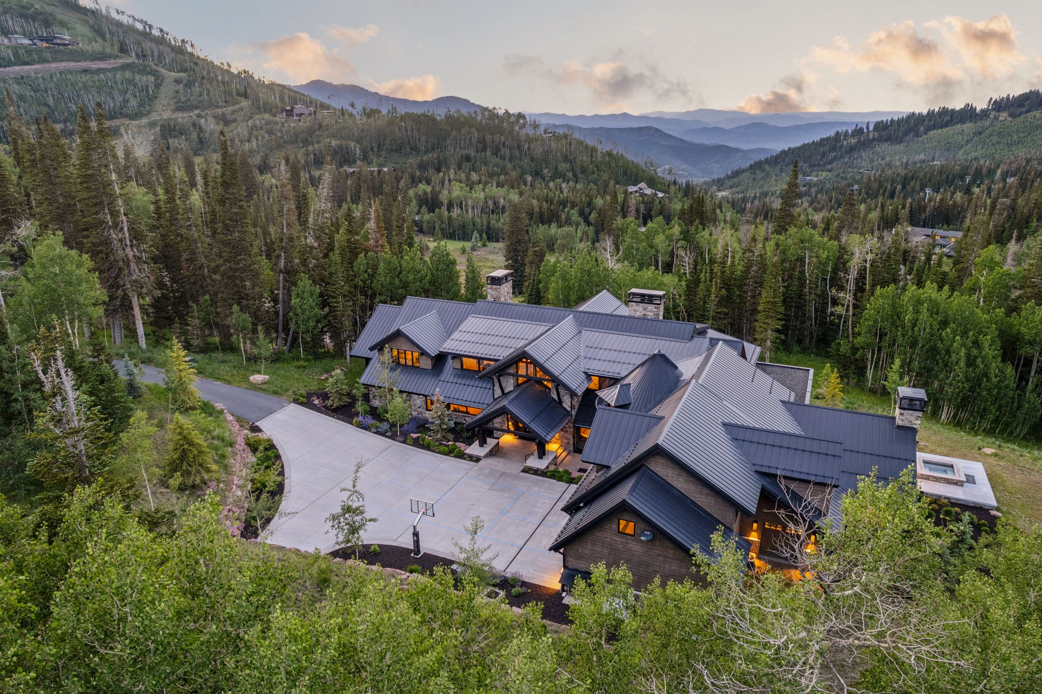 Mountain-modern residence featuring a dark metal roof, stone and wood siding, and multiple gables