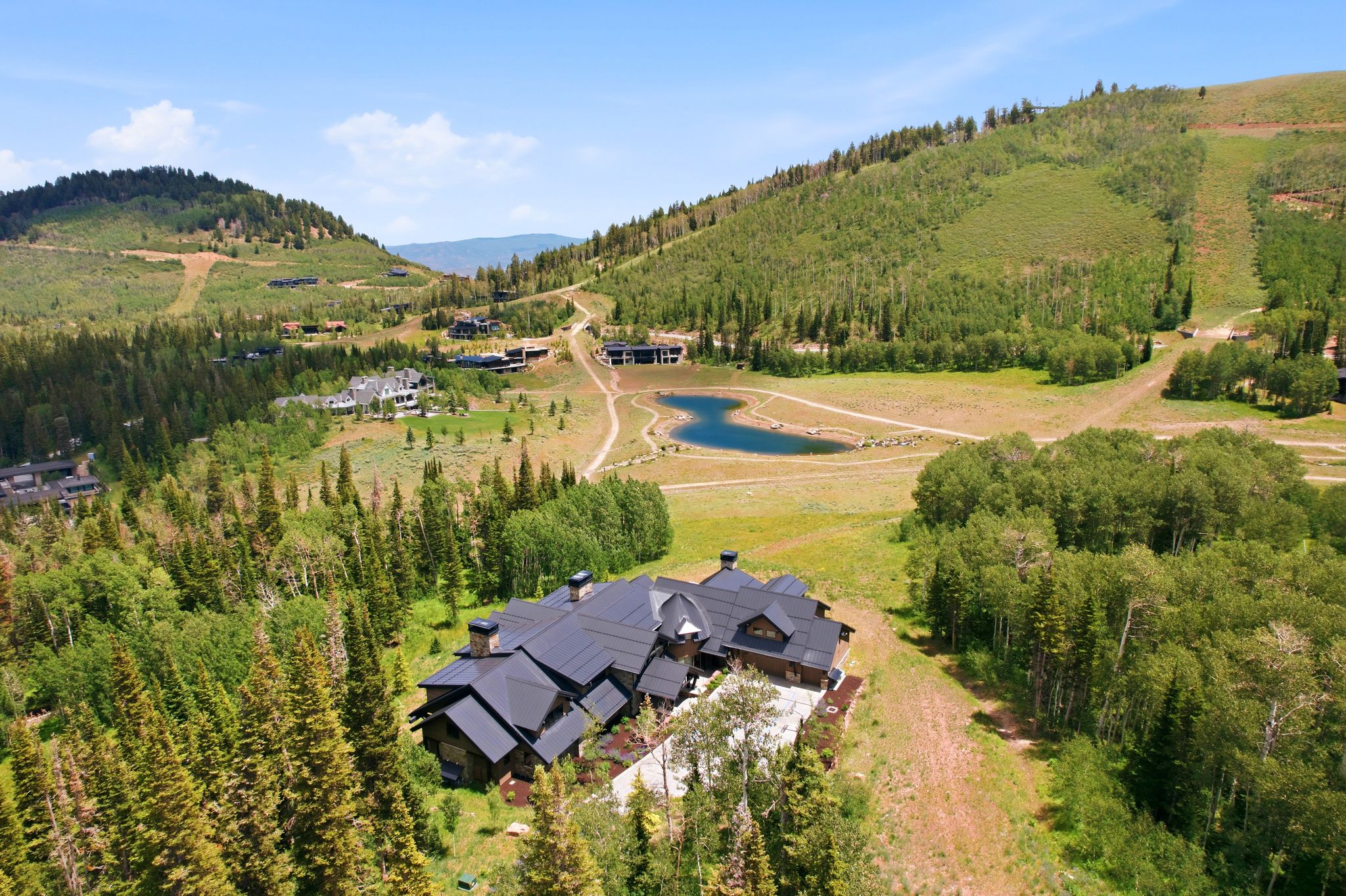 Expansive mountain property featuring a large residence with a multi-gabled roofline, surrounded by dense evergreen trees and natural landscaping