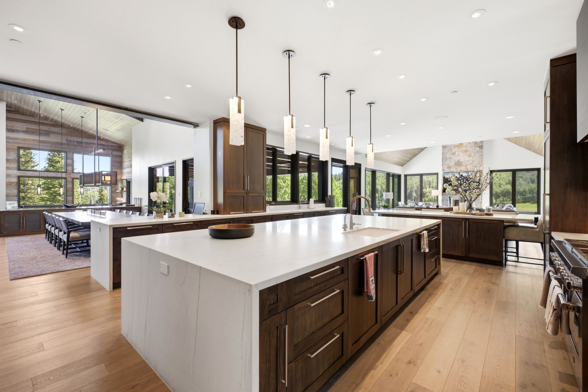 Expansive kitchen featuring a large central island with a sink, white countertops, dark wood cabinetry, and recessed lighting