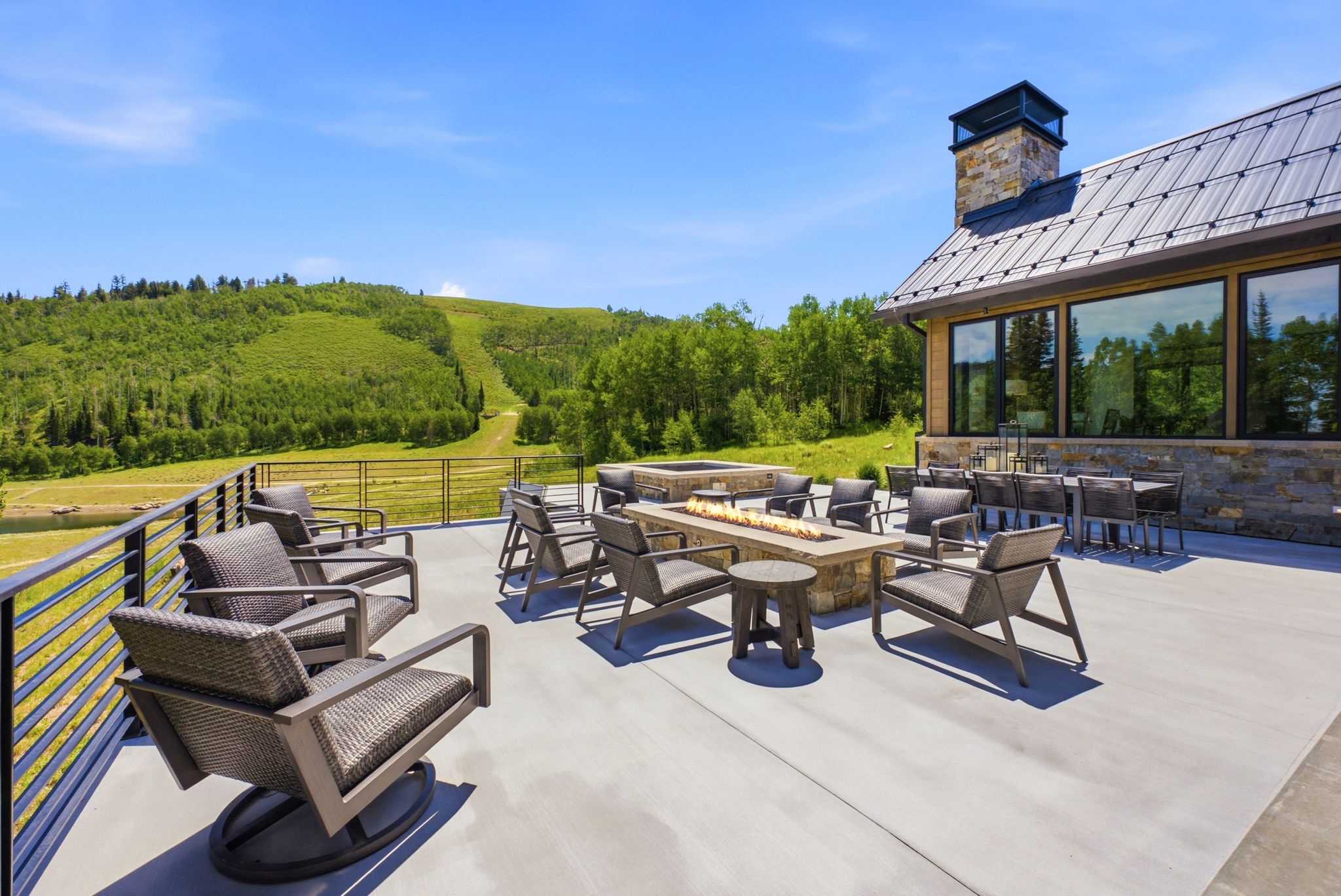 Expansive outdoor patio featuring a built-in linear fire pit, stone-clad chimney, and a metal standing seam roof