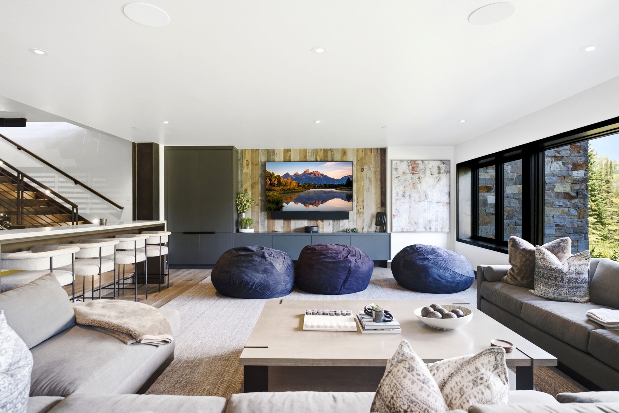 Spacious room featuring wood-finish flooring, a built-in bar with seating, a wood accent wall, and a large window with exterior stone cladding