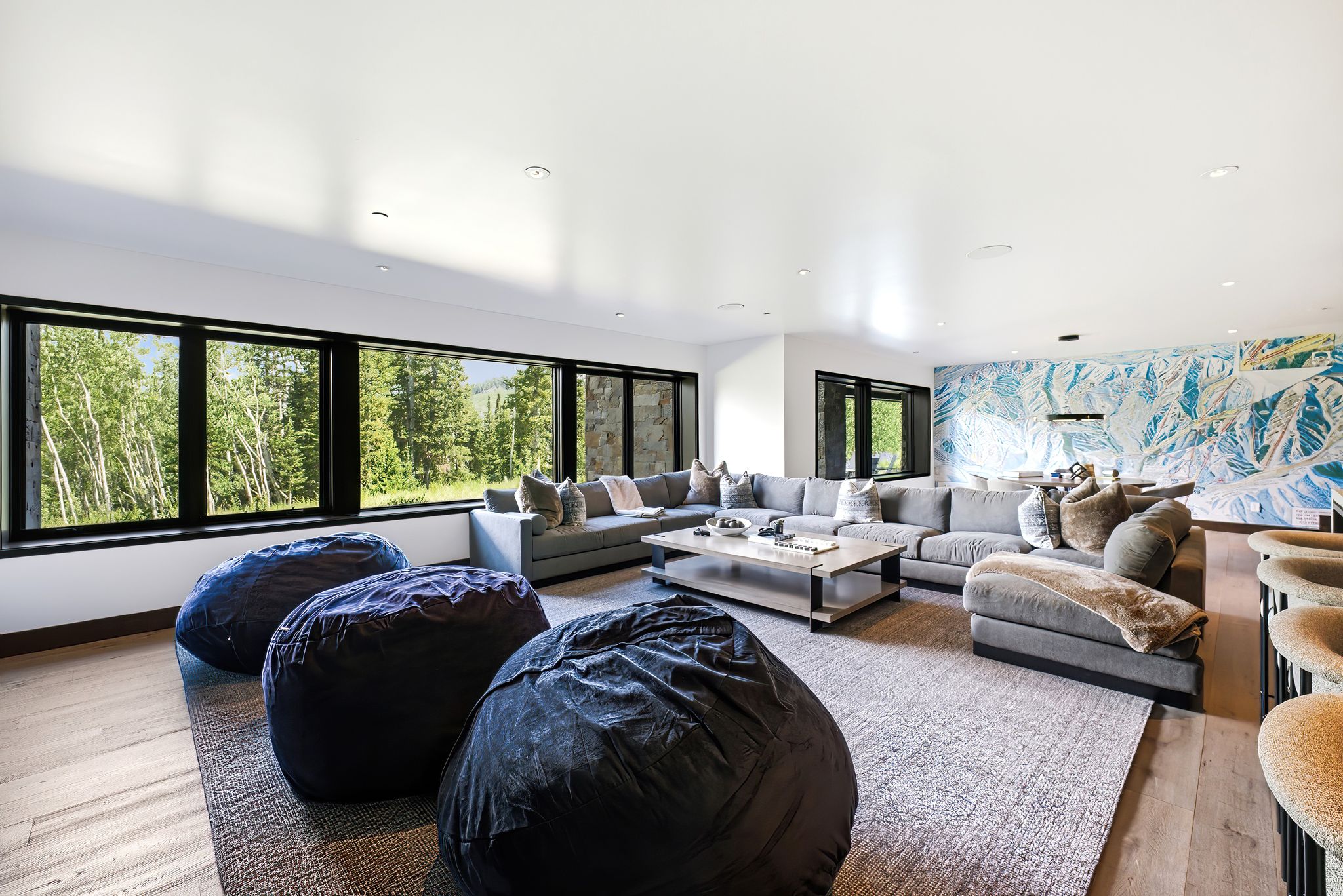 Expansive living area featuring a wall of black-framed windows, wood-finish flooring, recessed lighting, and a distinctive mural wall