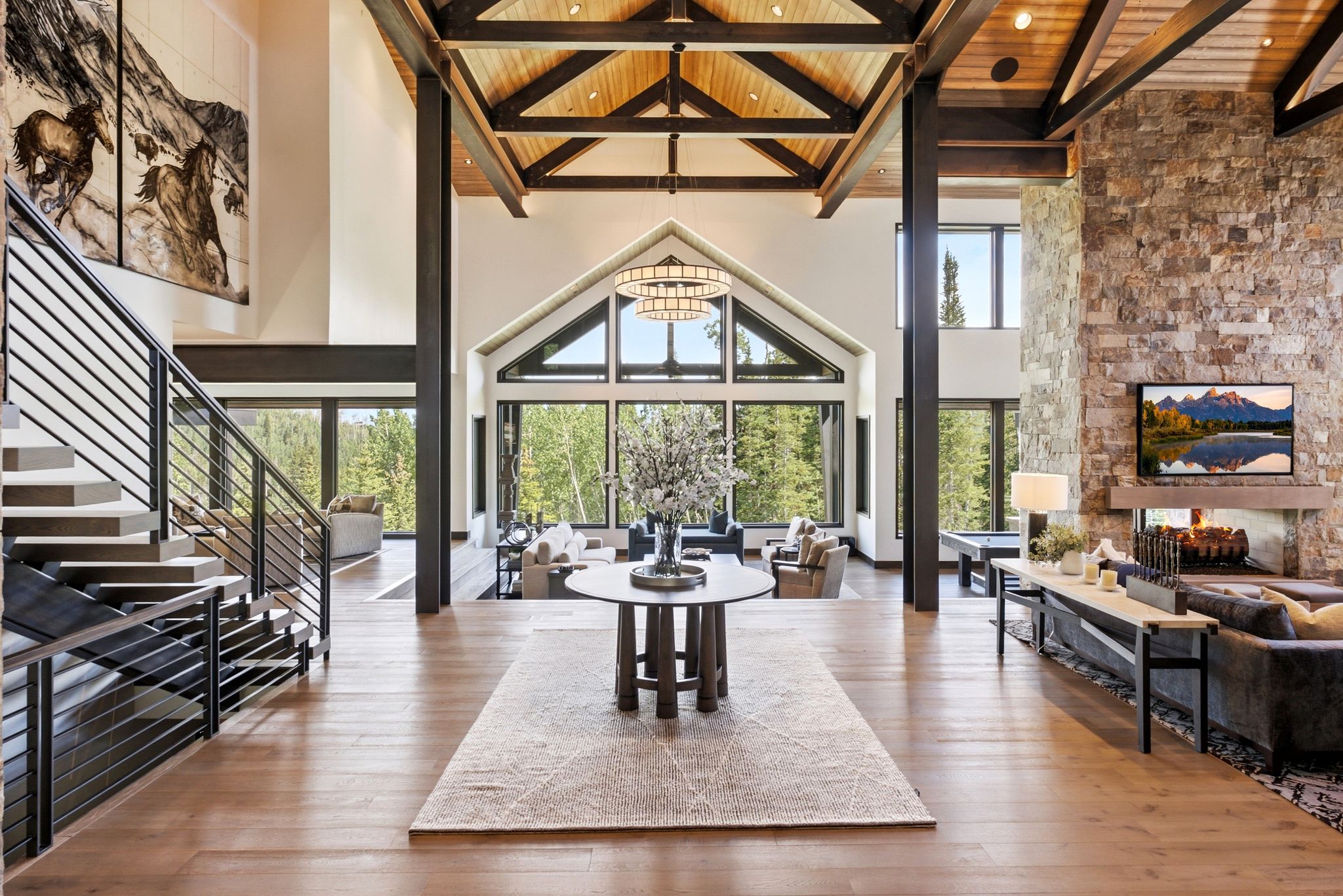 Grand foyer featuring wood-finish flooring, a contemporary staircase with metal railings, and a vaulted ceiling with exposed wood beams