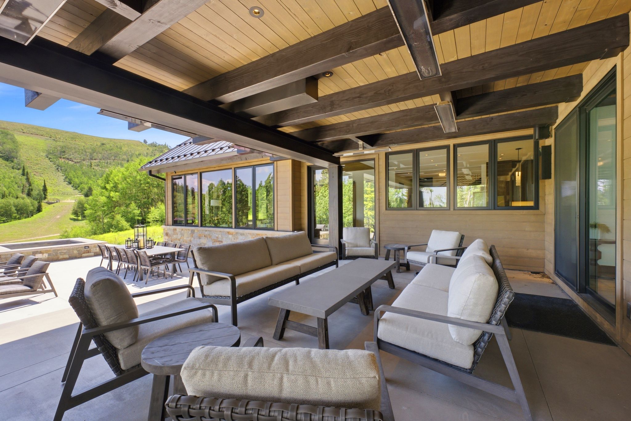 Expansive covered patio featuring a wood-finish ceiling with exposed beams, recessed lighting, and a stone-clad hot tub