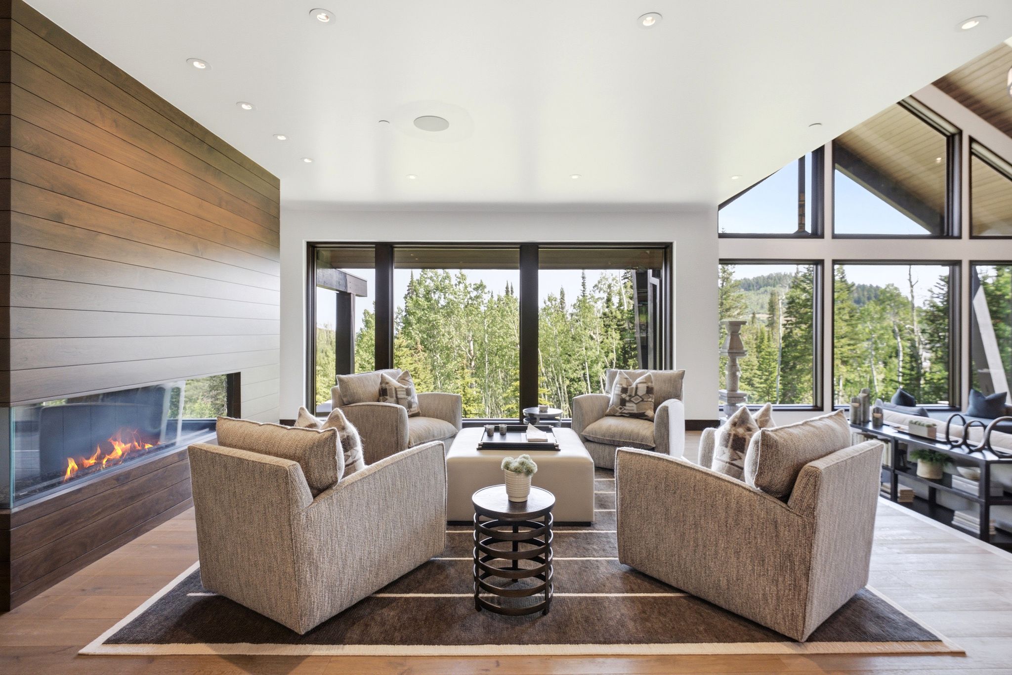 Open-concept living space with expansive floor-to-ceiling windows, showcasing a contemporary linear fireplace with a glass enclosure
