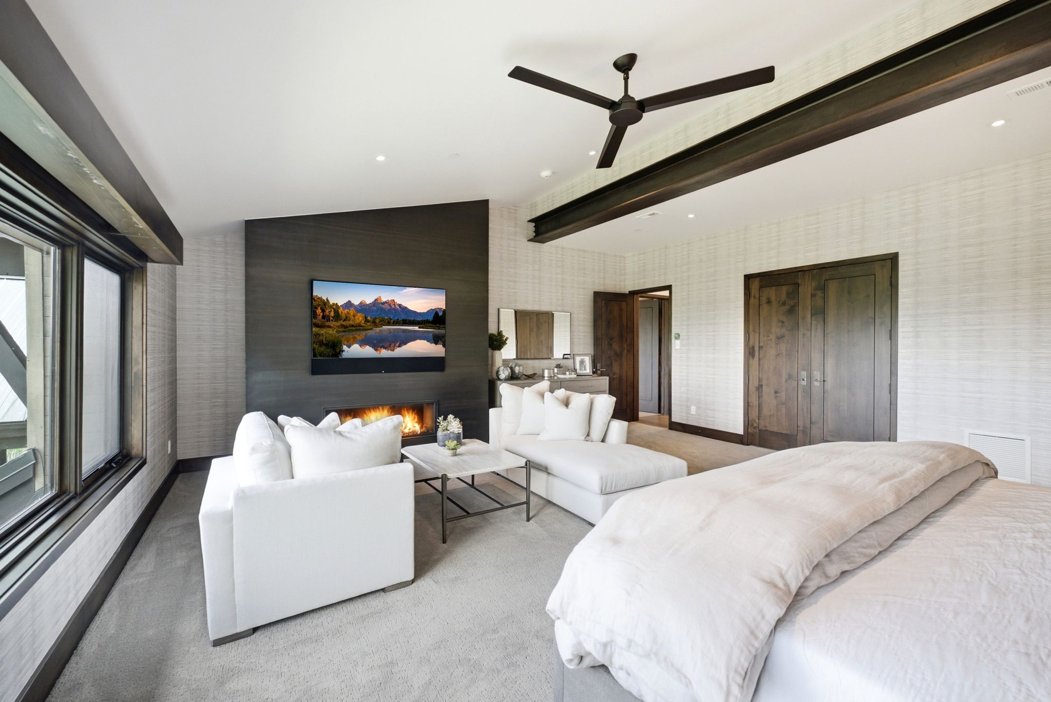 Spacious room featuring a linear fireplace, dark wood-tone accent wall, large windows, ceiling fan, and exposed ceiling beam
