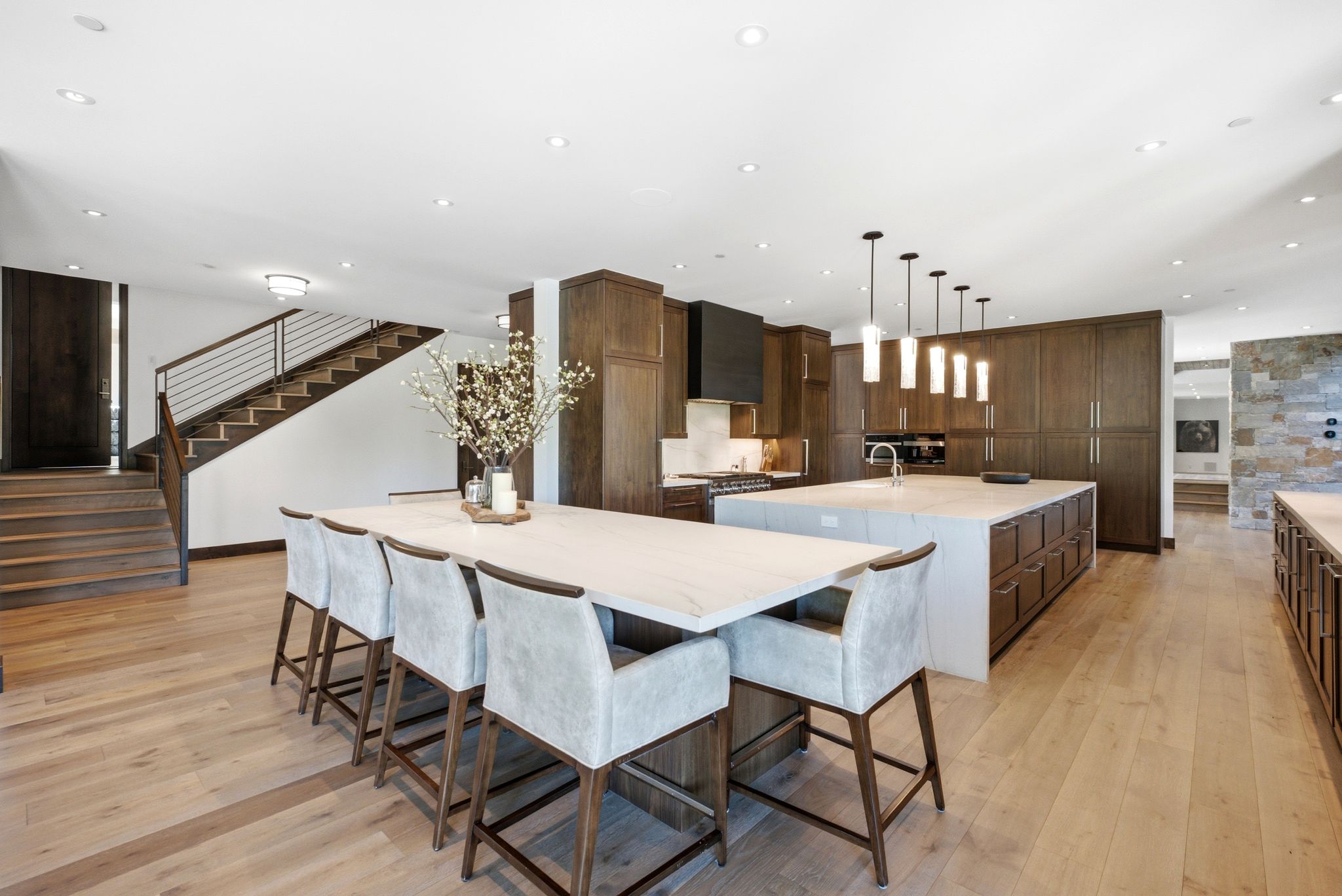 Open-concept kitchen featuring an expansive island with seating, dark wood cabinetry, integrated appliances, and light wood-finish flooring