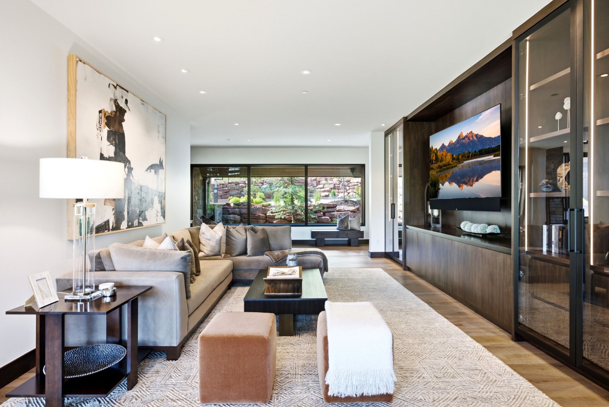 Spacious interior featuring a built-in media console, dark wood-finish flooring, recessed lighting, large windows, and an abstract wall art piece