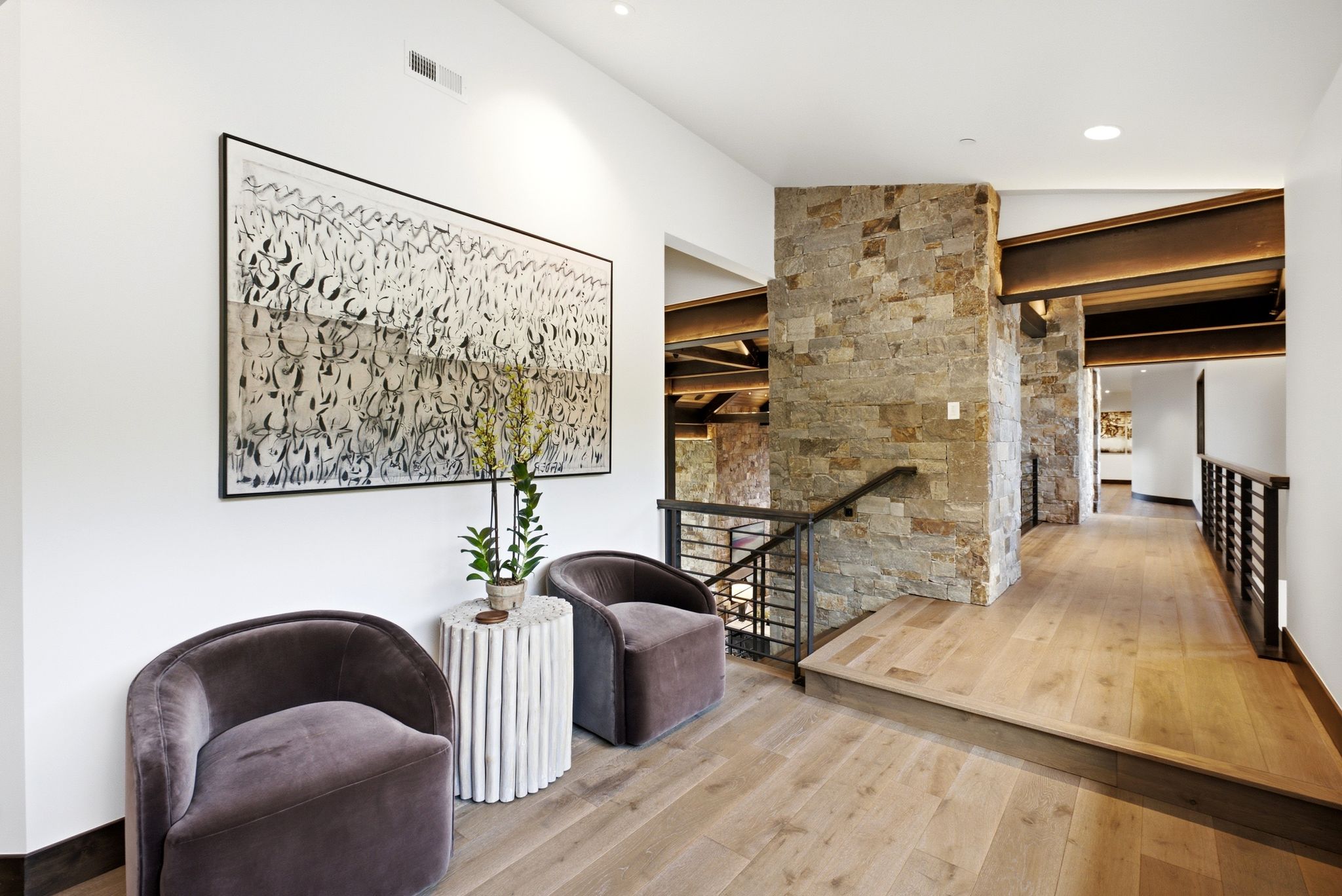 Open hallway featuring natural wood-finish flooring, exposed structural beams, and stone-clad architectural elements