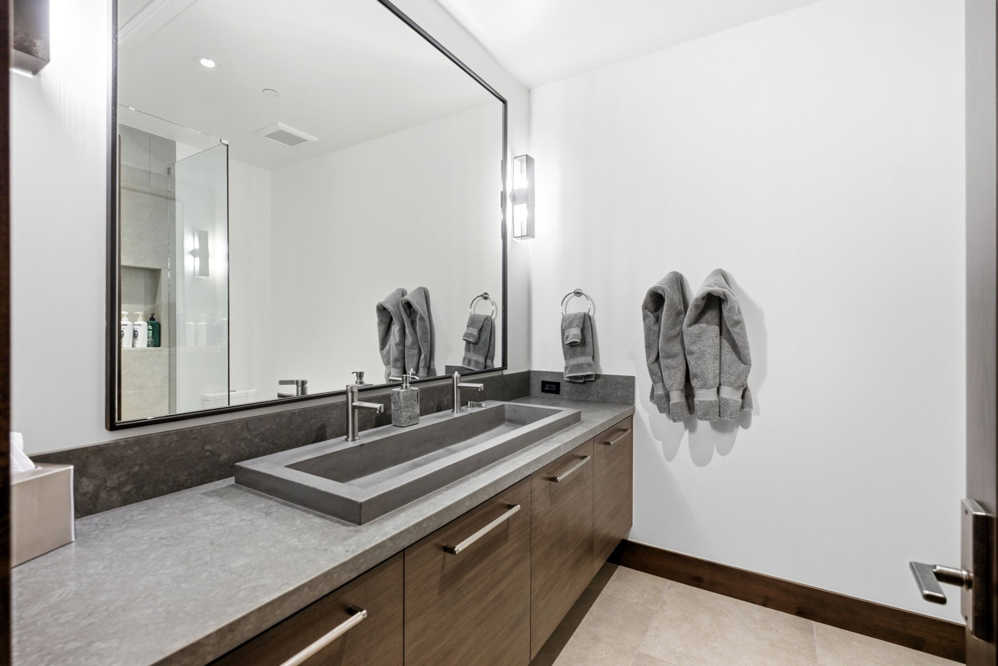 Dual-faucet trough sink with a stone countertop and wood-finish cabinetry