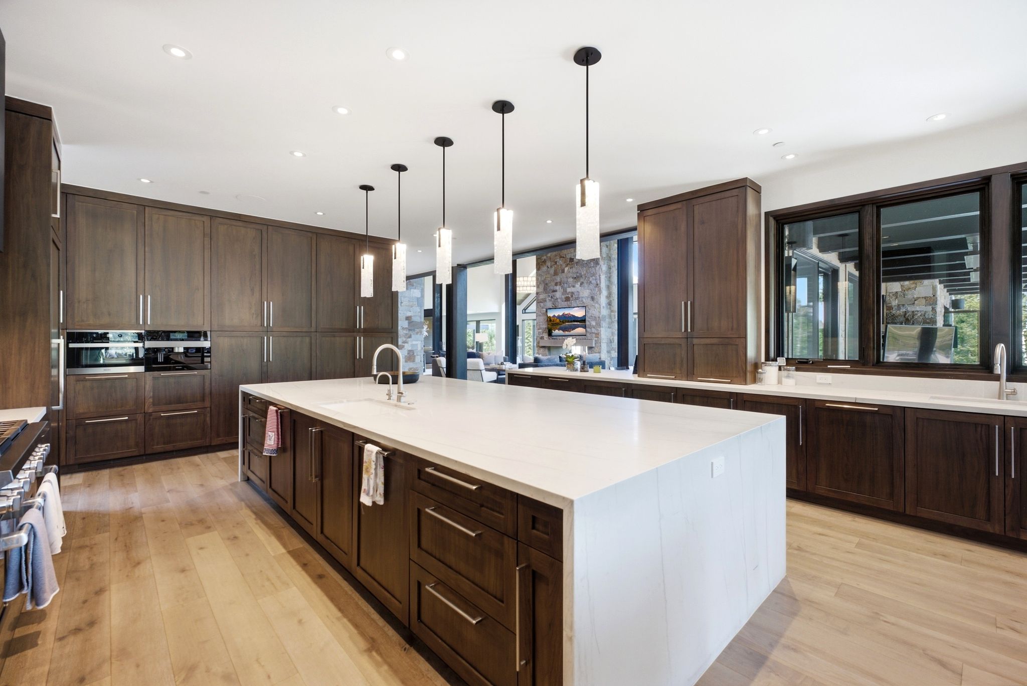 Gourmet kitchen featuring a large waterfall island with an undermount sink, pendant lighting, custom wood cabinetry, integrated appliances, and light wood-finish flooring