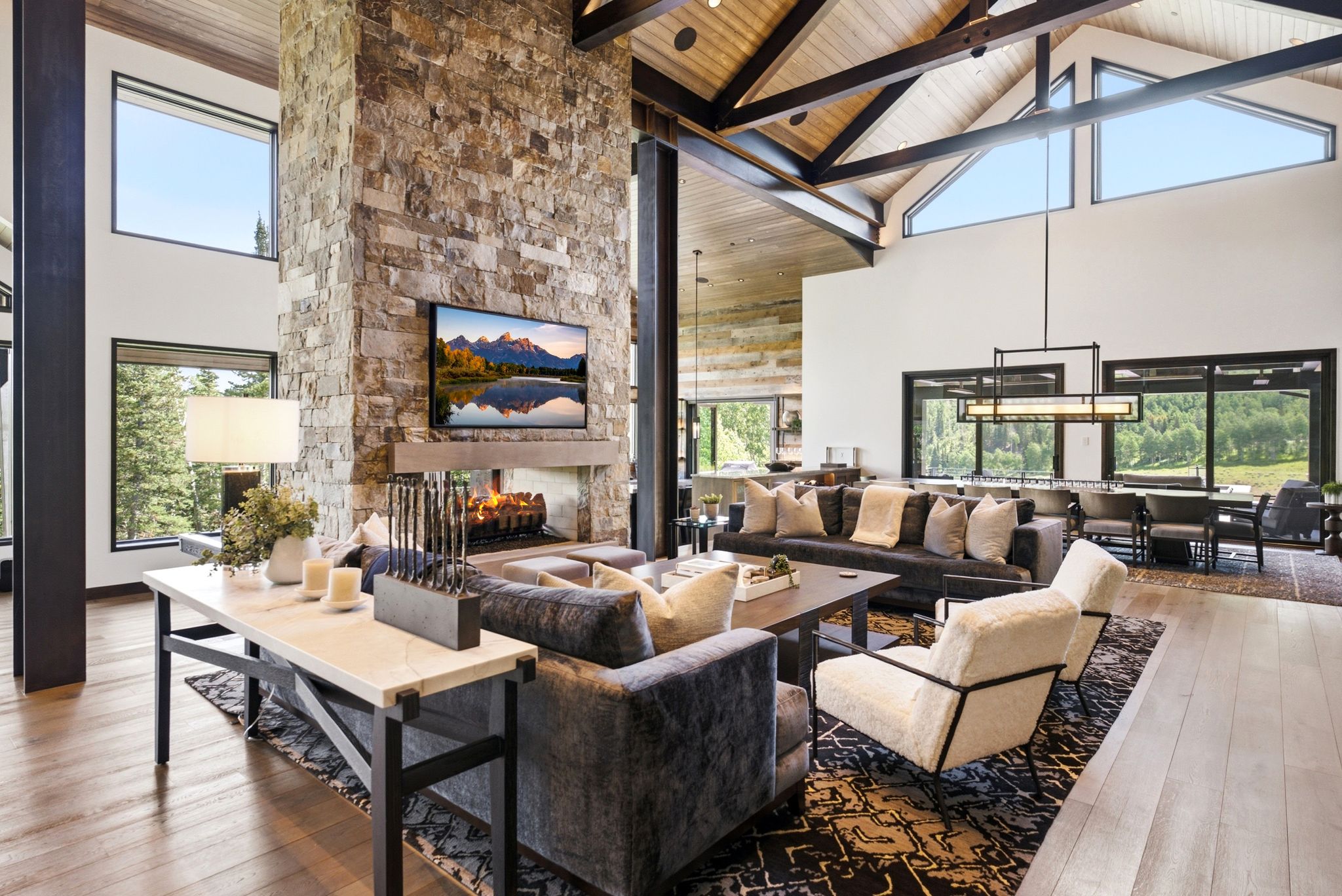 Great room featuring a floor-to-ceiling stone fireplace, soaring vaulted wood-paneled ceilings, exposed wood beams, and expansive windows
