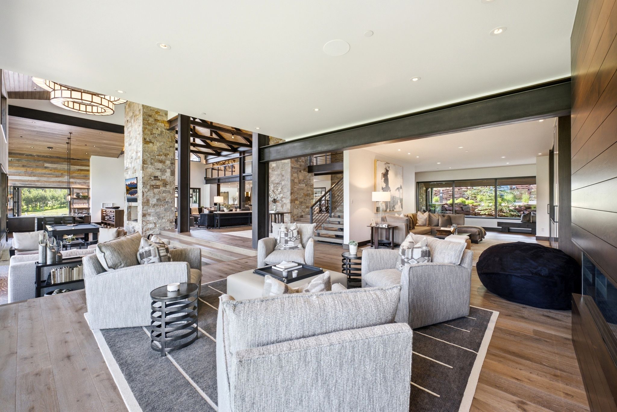 Spacious great room featuring wood-finish flooring, stone accent walls, exposed beams, and a modern fireplace with wooden paneling