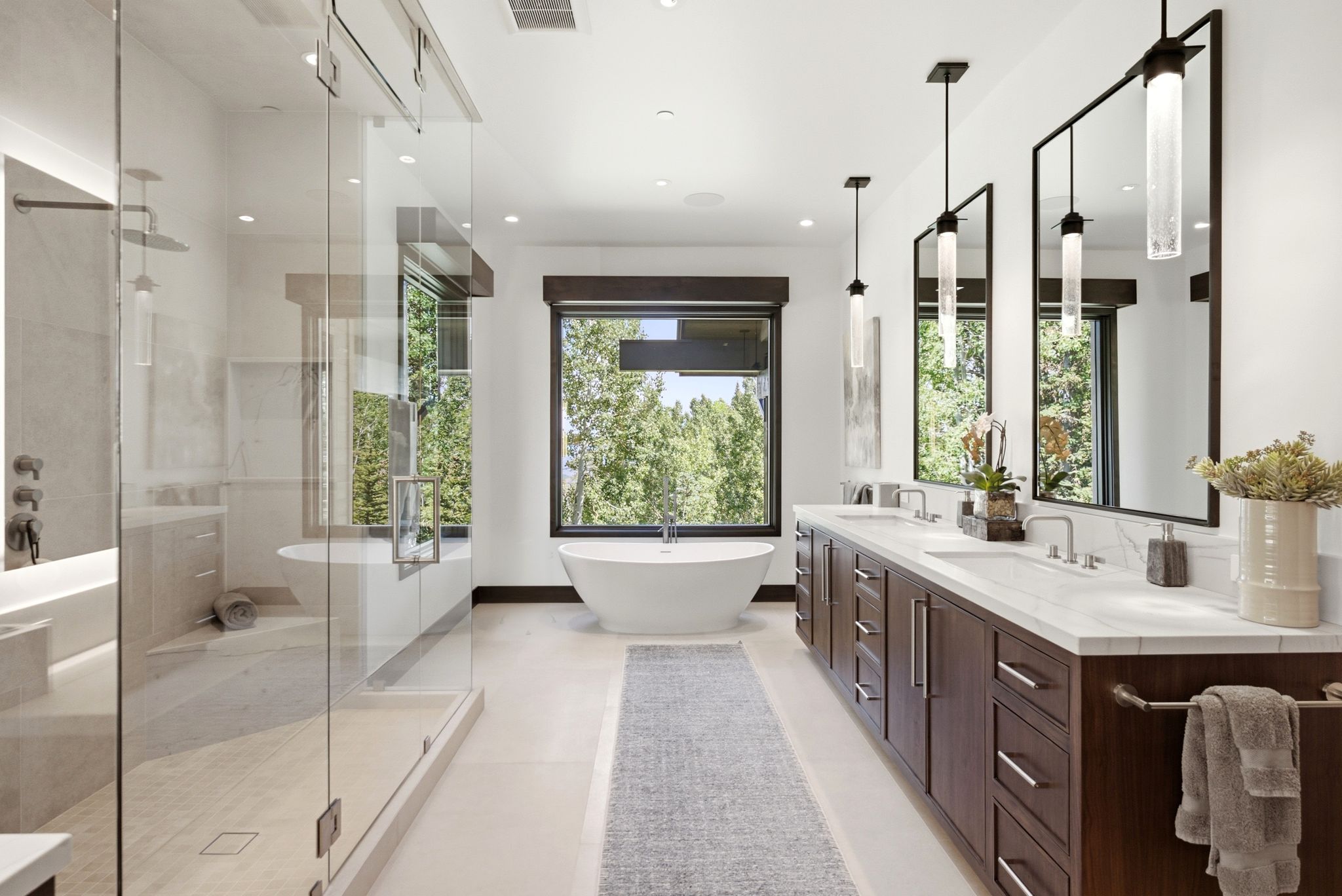 Sleek bathroom featuring a dual vanity with wood-finish cabinetry and light-toned countertops, a freestanding soaking tub, and a spacious glass-enclosed shower