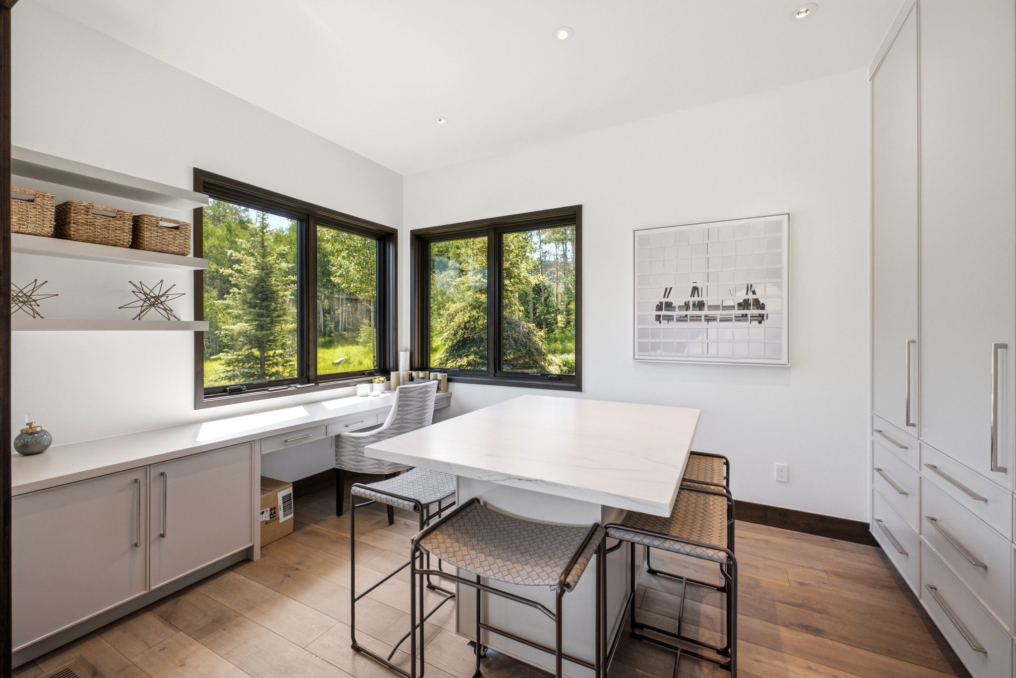 Home office featuring extensive built-in cabinetry, wood-finish flooring, and multiple windows with dark frames
